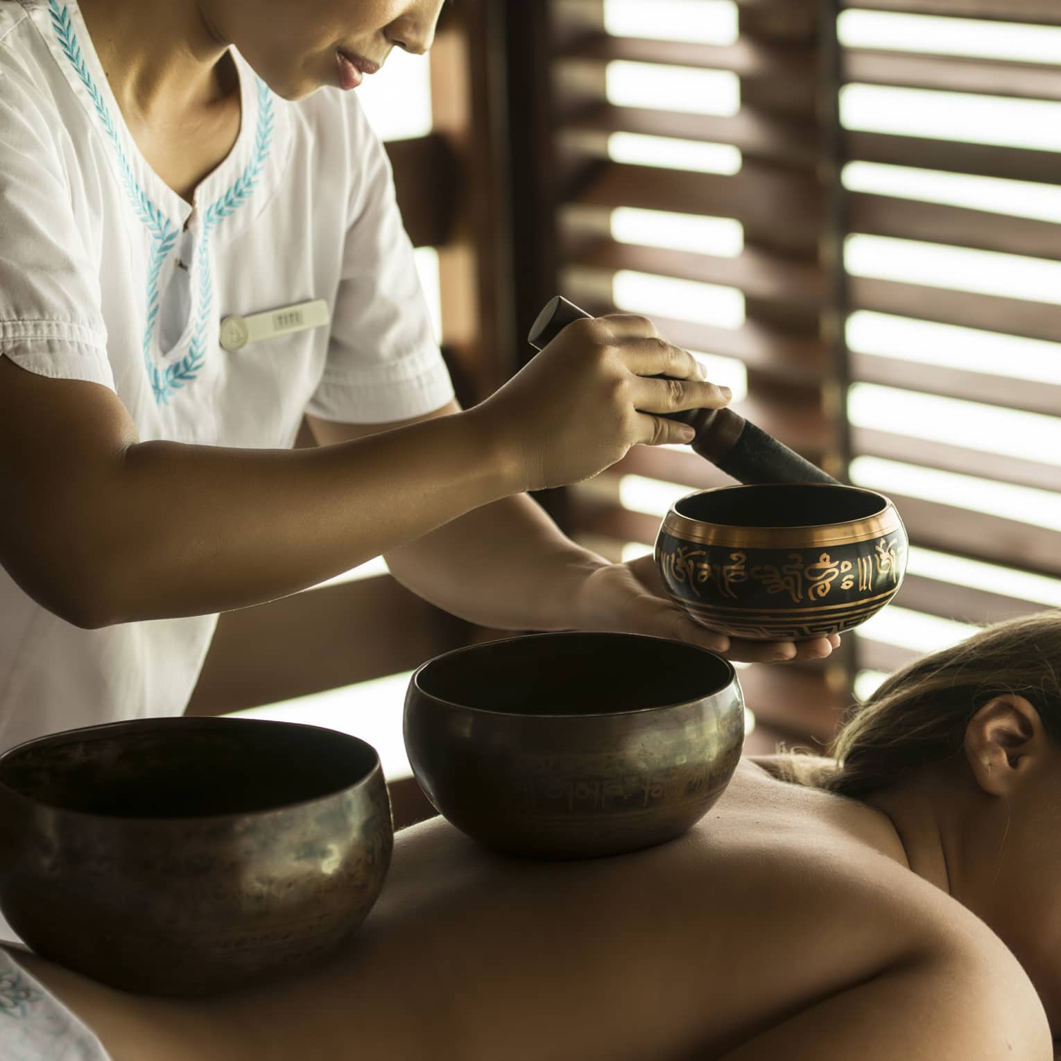 Therapist performing a sound healing ritual with singing bowls on a relaxed spa guest