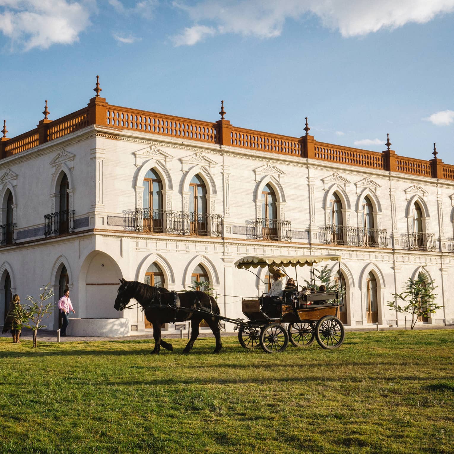 Guests enjoying a horse-drawn carriage ride around a large white building with several beautifully carved arched doorframes.