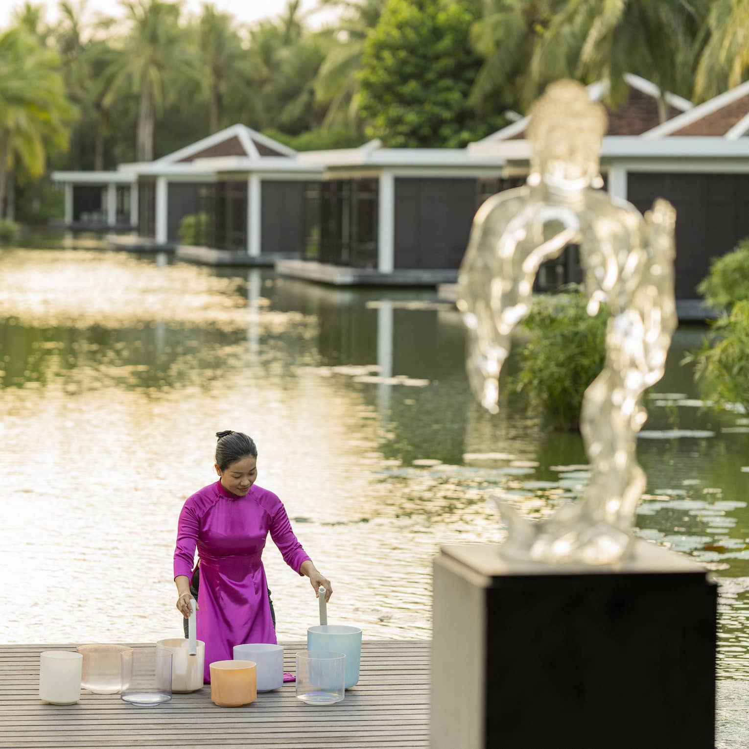 Woman plays crystal singing bowls on the dock of the lake