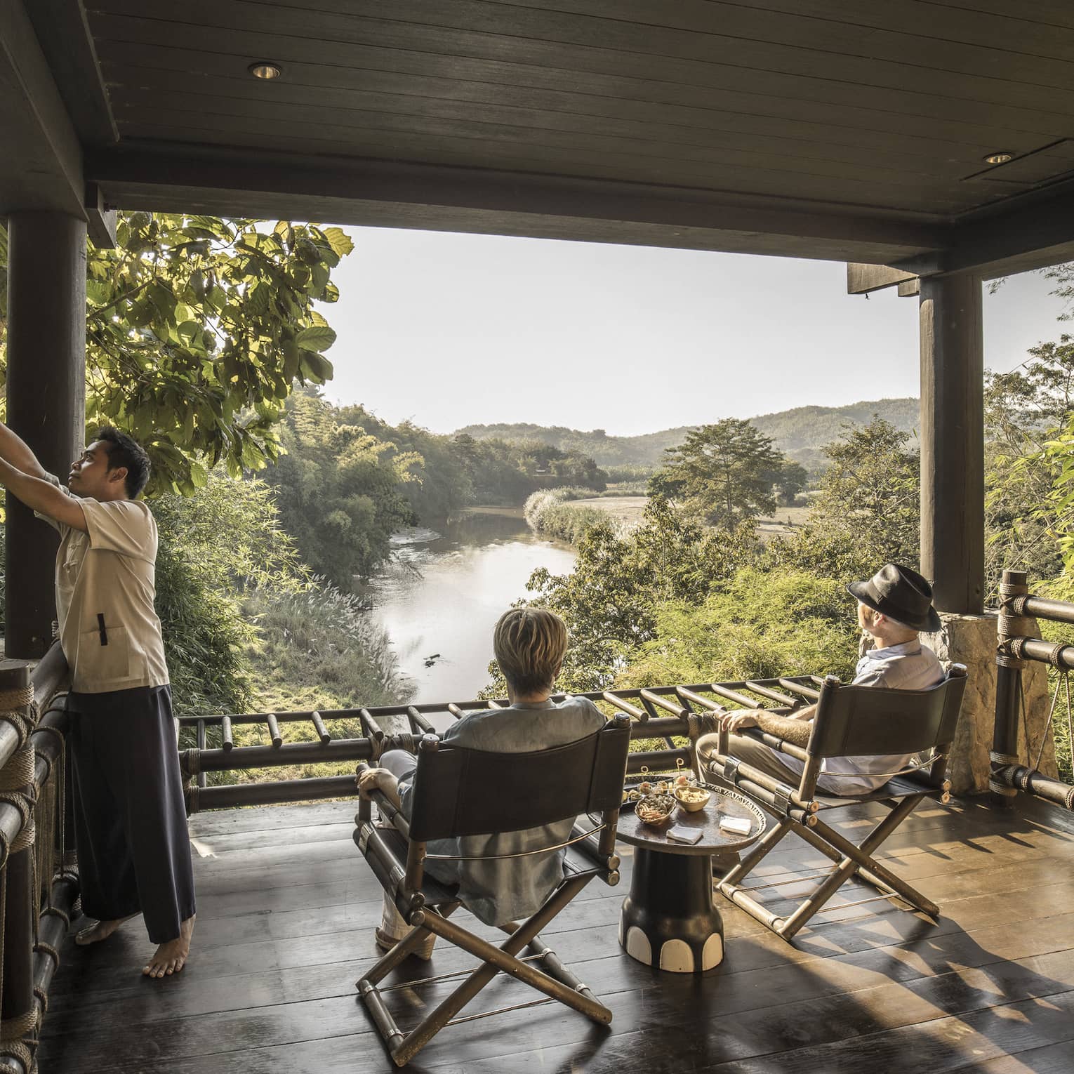 Couple, hotel staff on wood platform patio overlooking the lush Ruak River basin