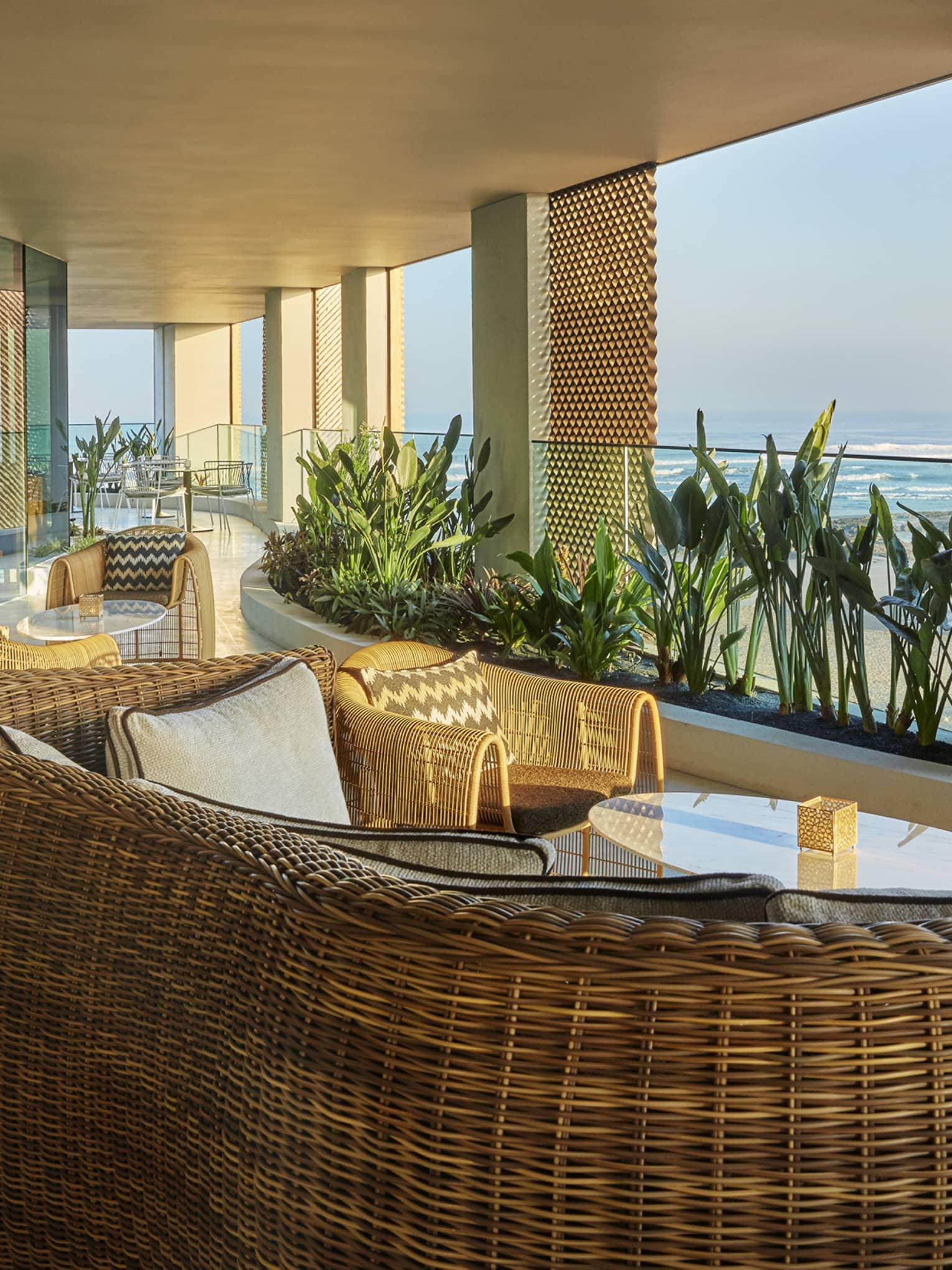 Bleu patio with large wicker sofas, chairs, tropical plants, beach views