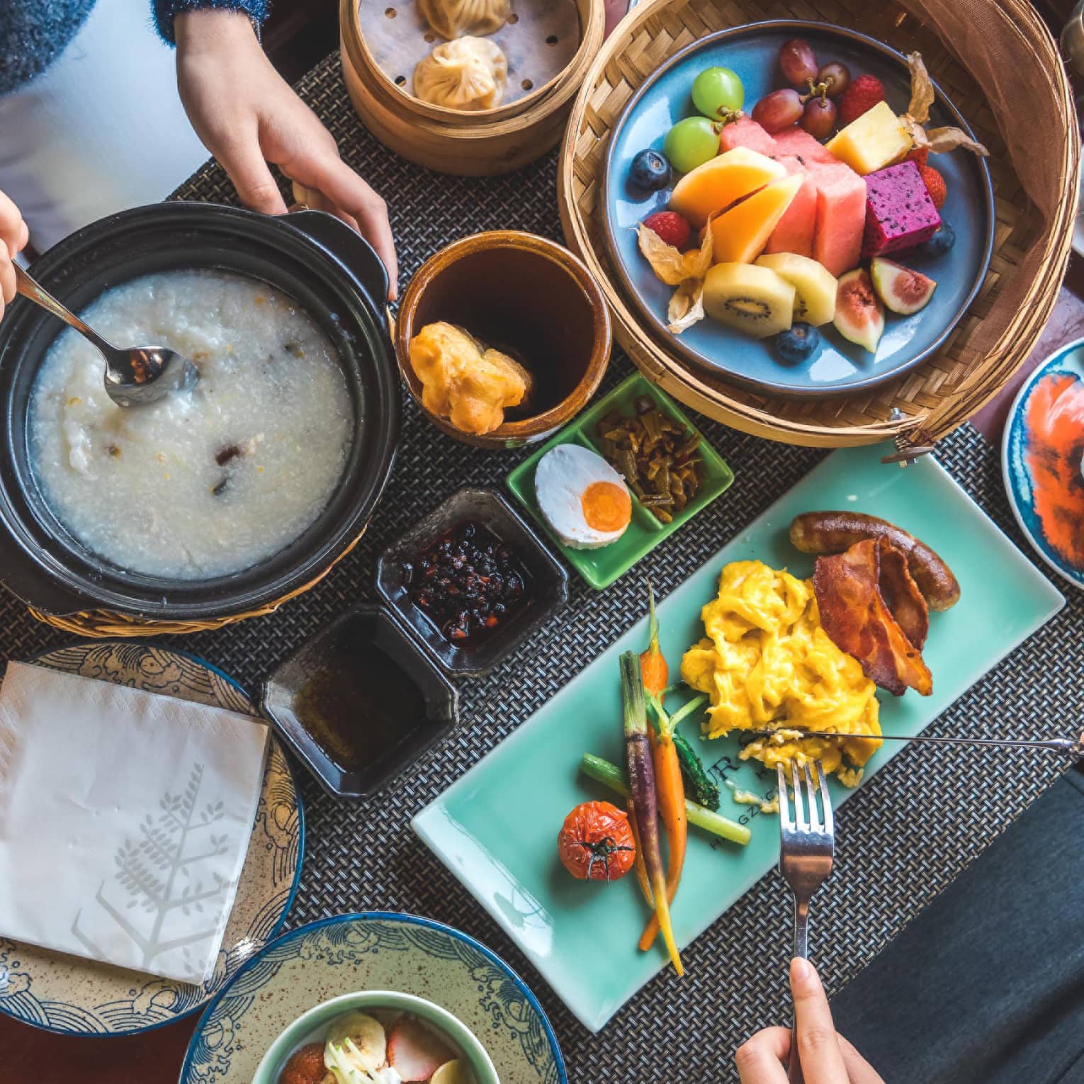 View from above as two guests savour a sumptuous array of vibrant dishes, including pastries, congee, fresh fruit and coffee.