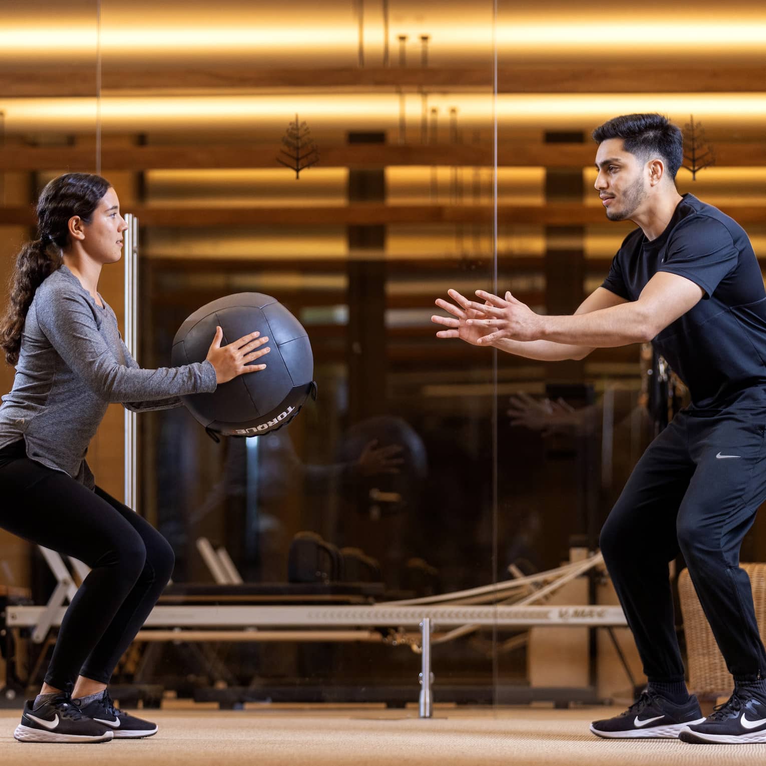 Two people exercise with an exercise ball in an indoor fitness centre setting.