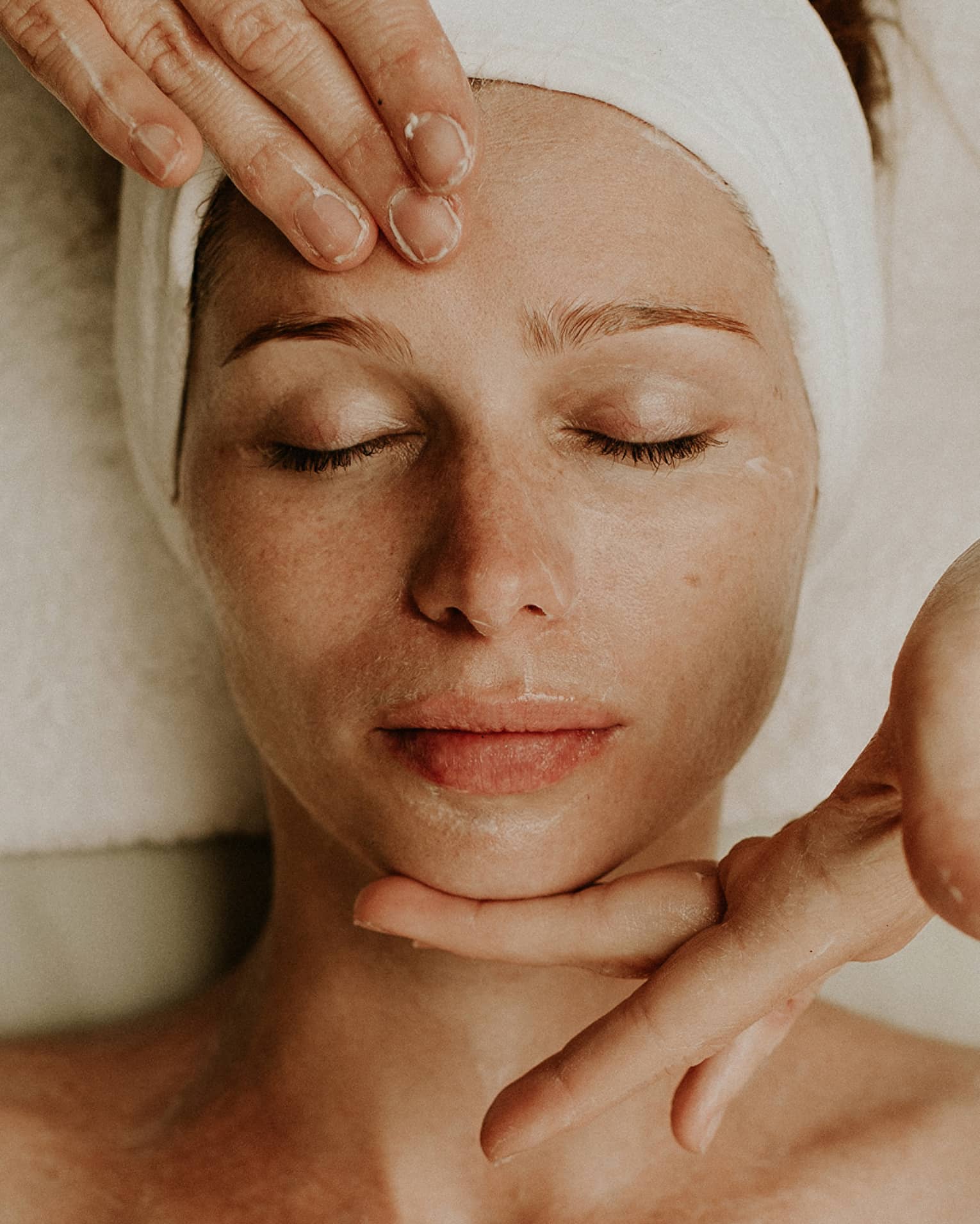 Person receiving a relaxing facial massage with eyes closed and head wrapped in a towel