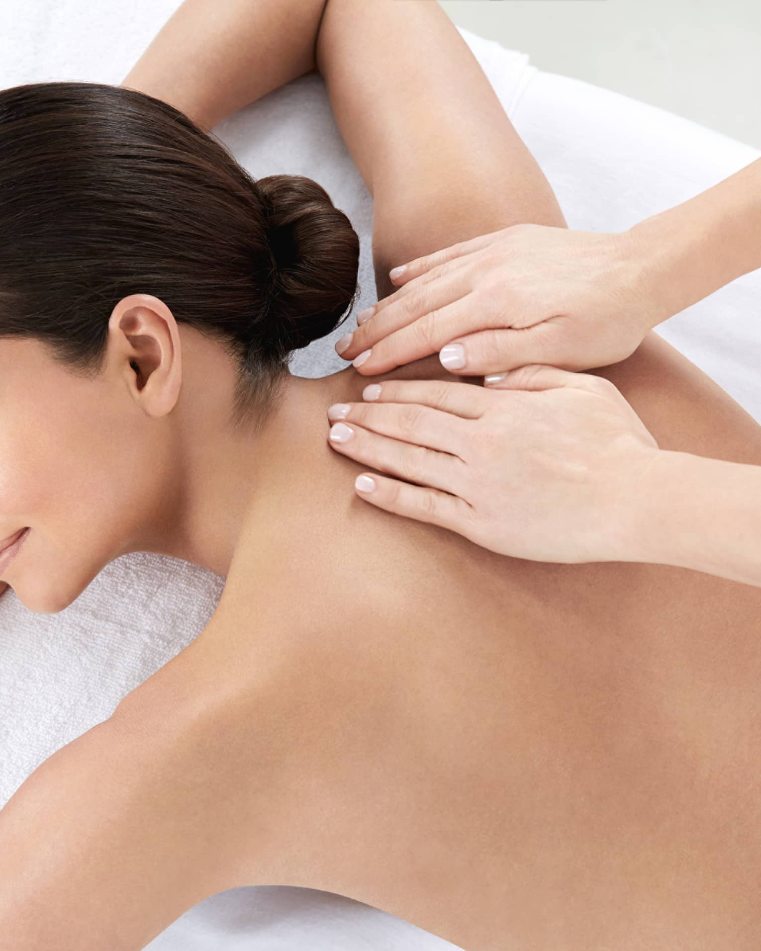 Woman smiles, lies on massage table as hands massage bare shoulders