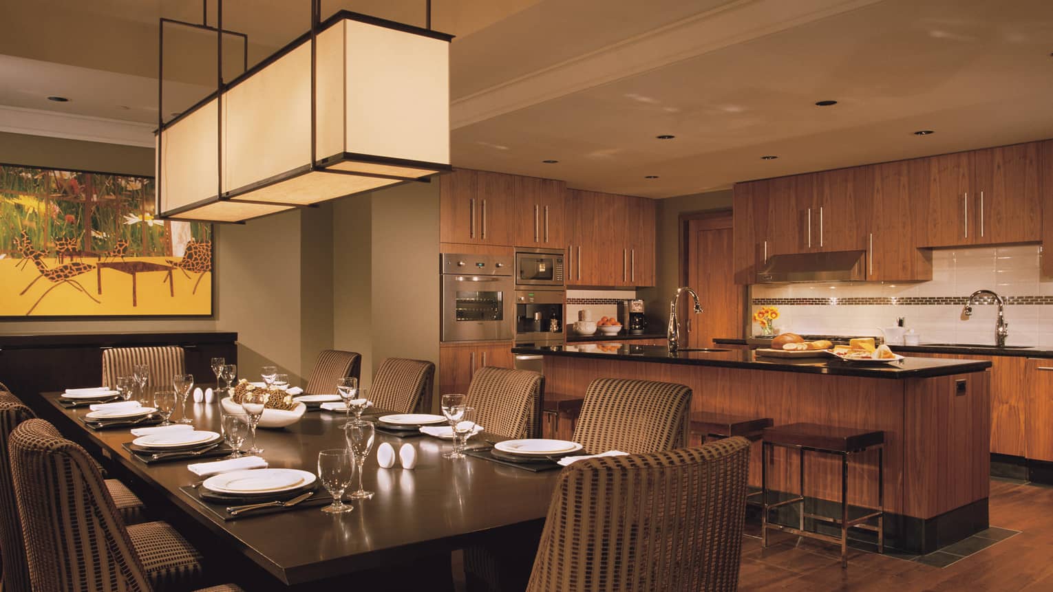 Long lantern chandelier over private dining table in front of kitchen counter with bread, cheese