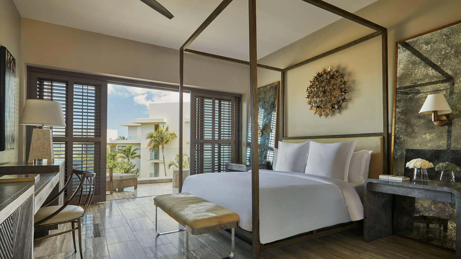 Resort View Room with canopy bed, small brown leather bench, desk, patio doors with wood shutters