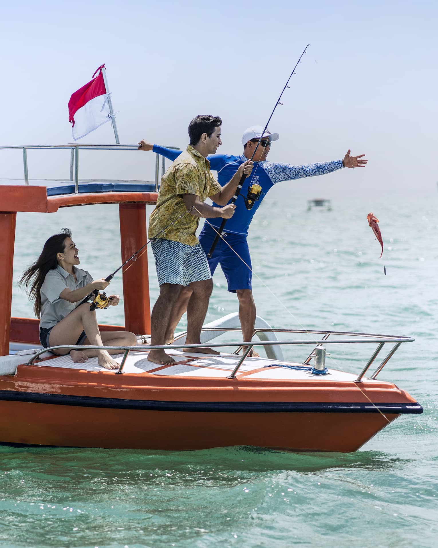 Tour guide teaches two guests to fish on a traditional jukung fishing boat on the open ocean
