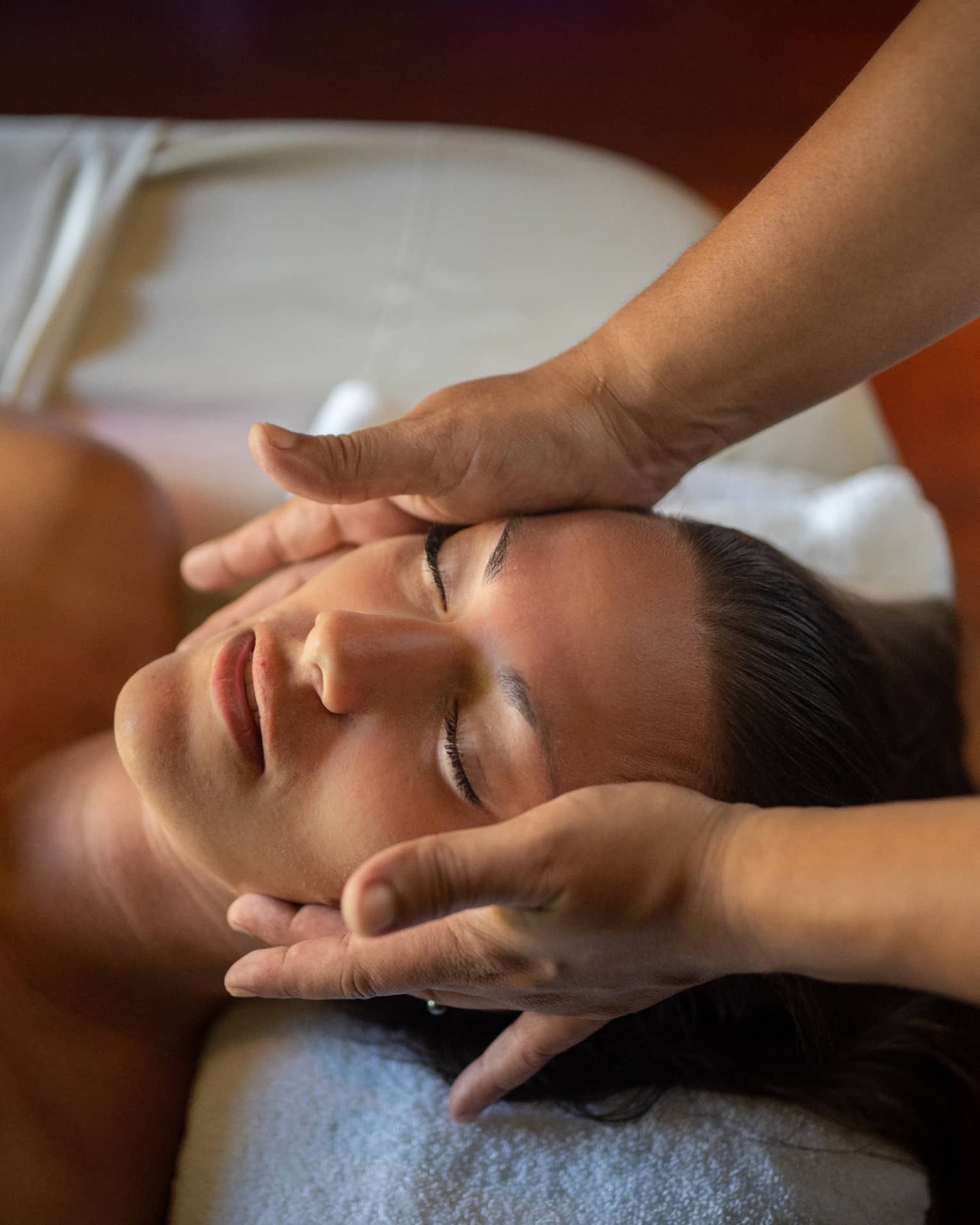 Woman lays on massage table with eyes closed as hands massage her cheeks and chin