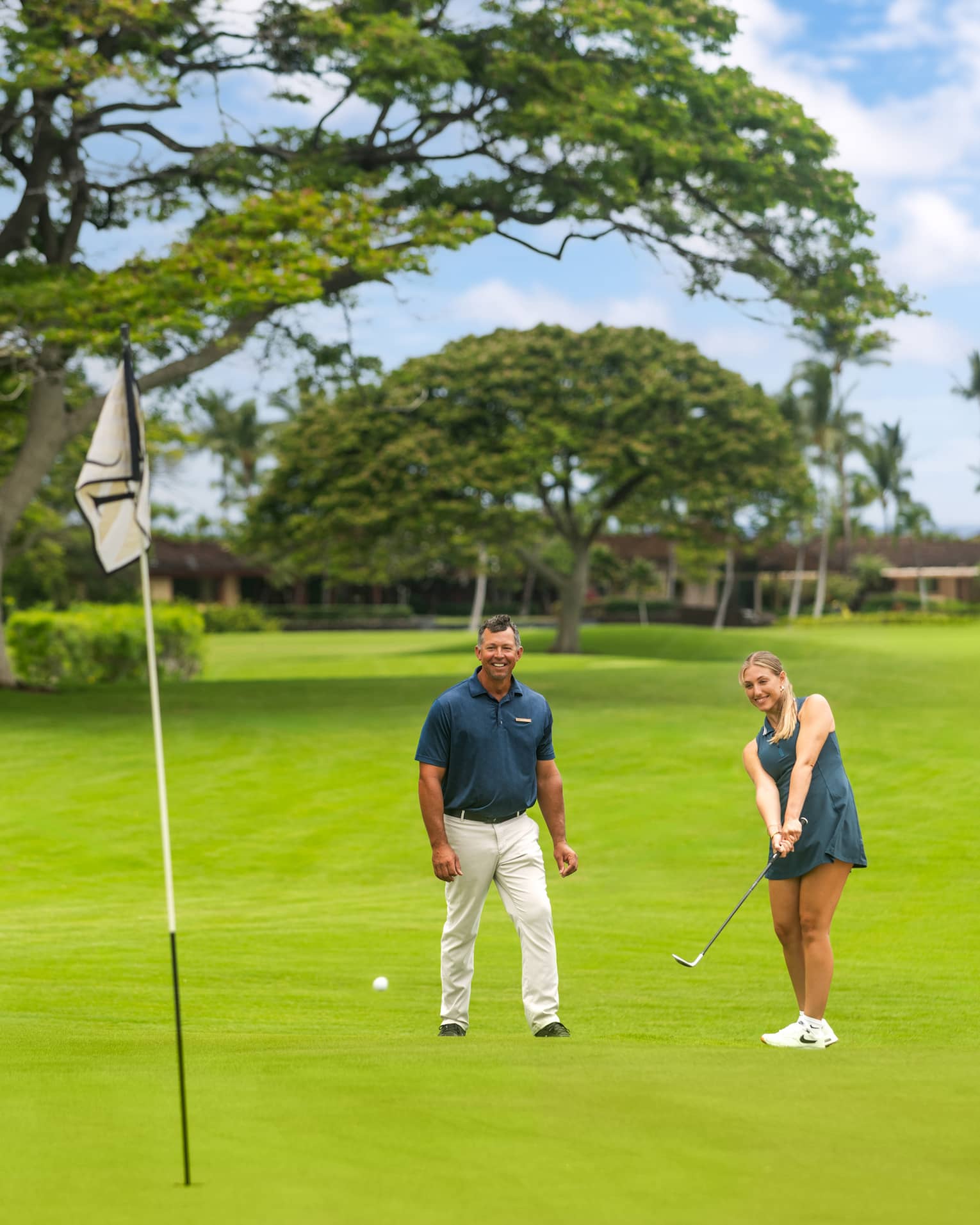 Two people on a golf course with one practicing her short game.