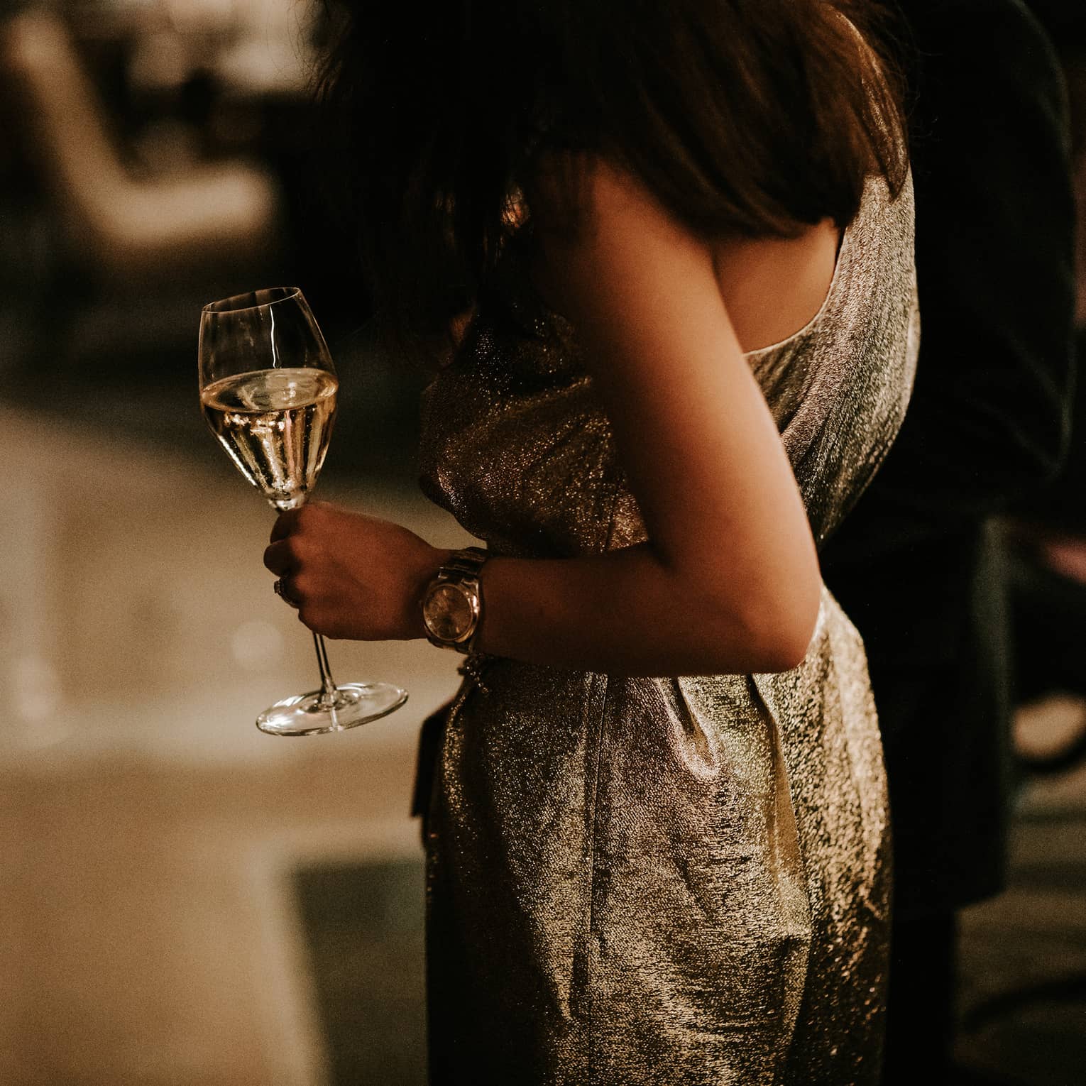 Woman in gold dress holding a glass of white wine