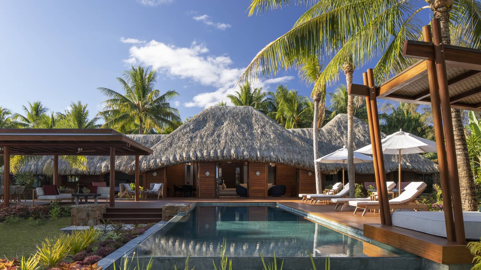 Private pool in a villa, with white sun chairs and a thatched-roof patio
