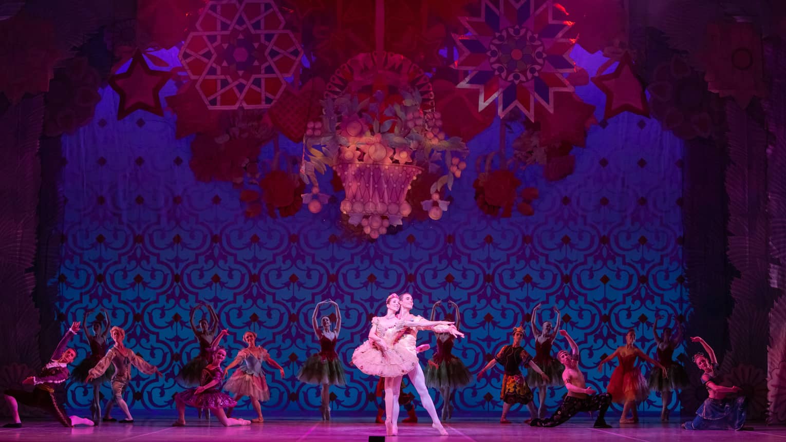 Two dancers performing ballet with back up dancers behind them in a red and blue scene.