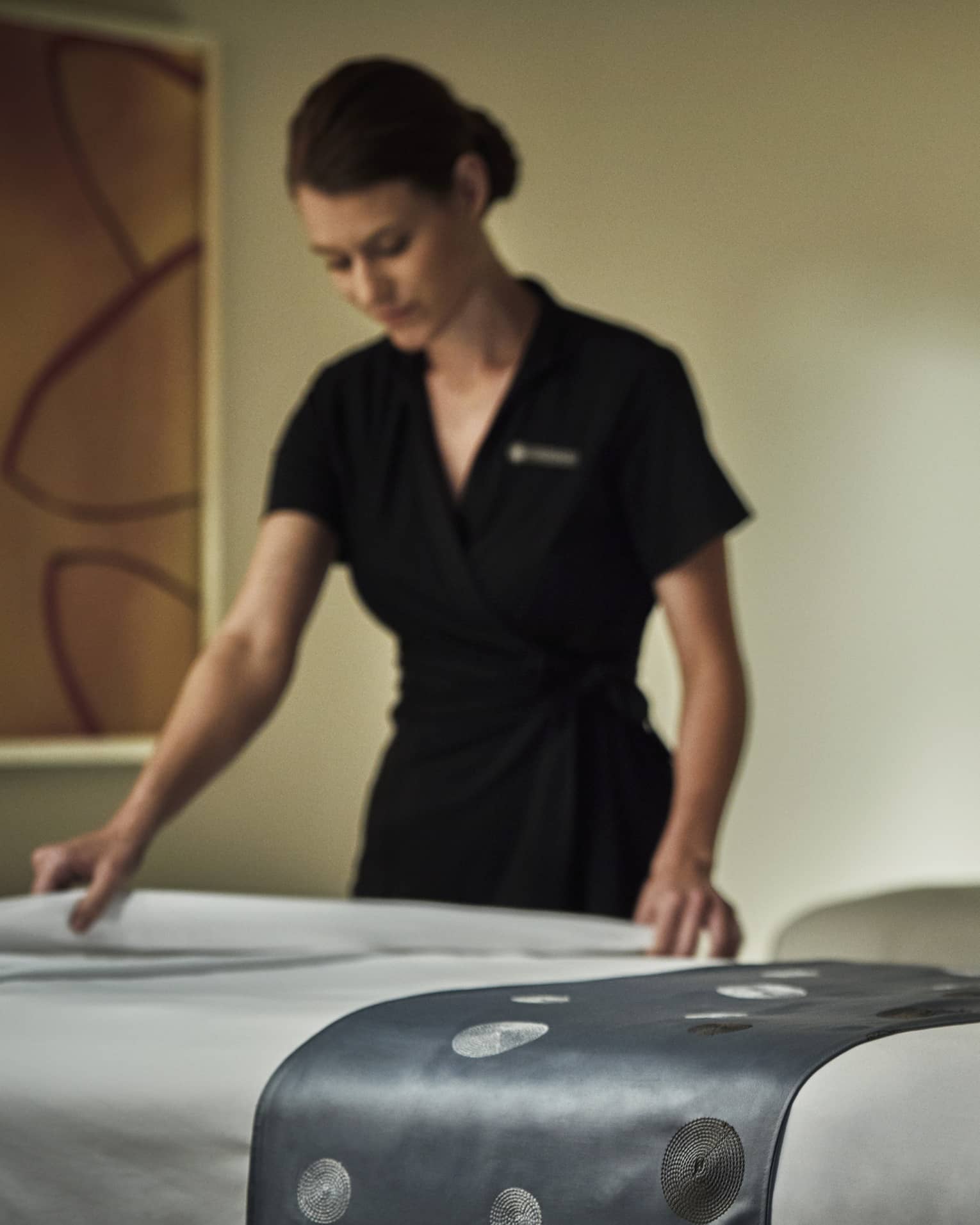 Spa attendant in black dress folds down white sheet on massage table