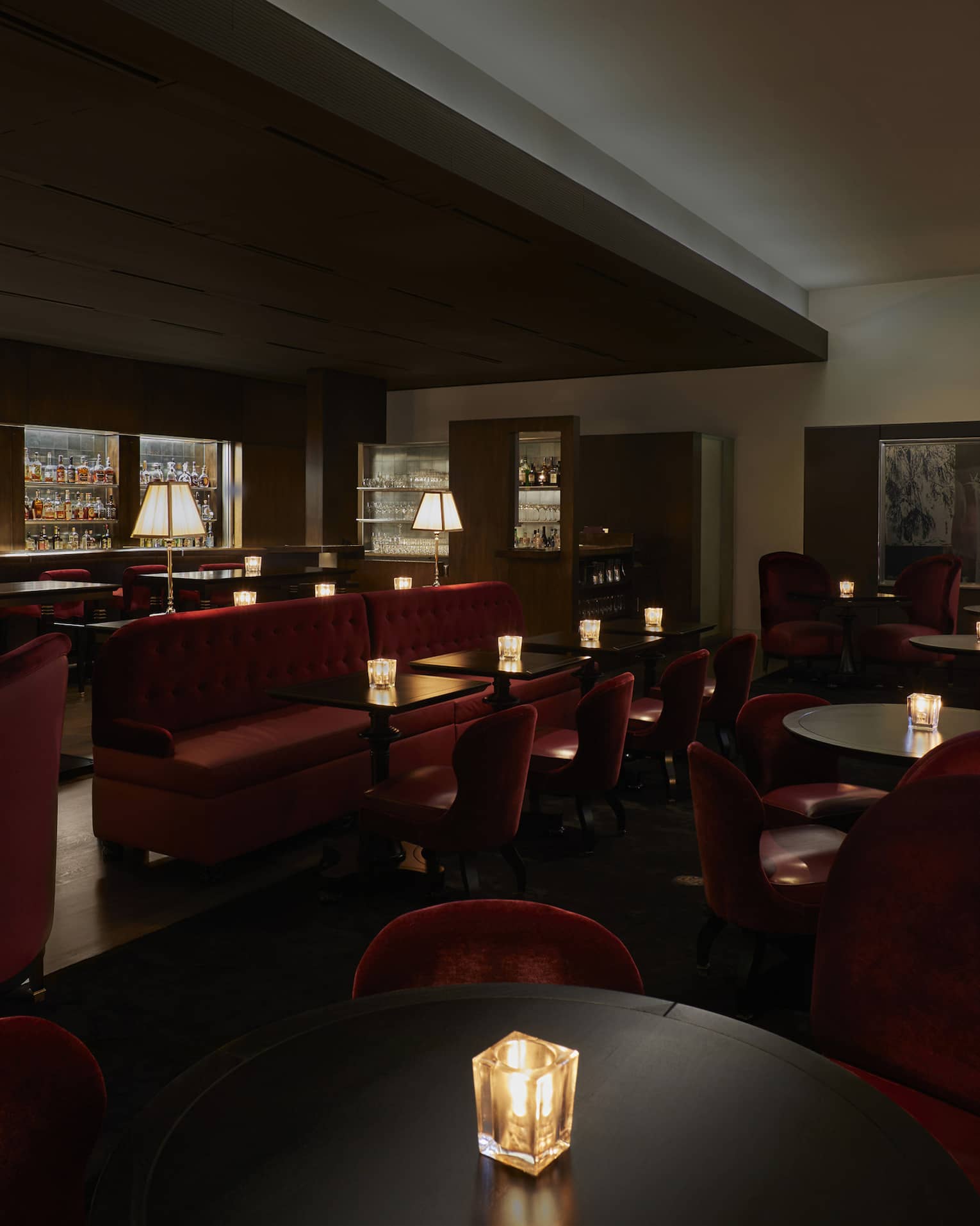 A dimly lit lounge with red chairs and a large selection of drinks behind a bar.