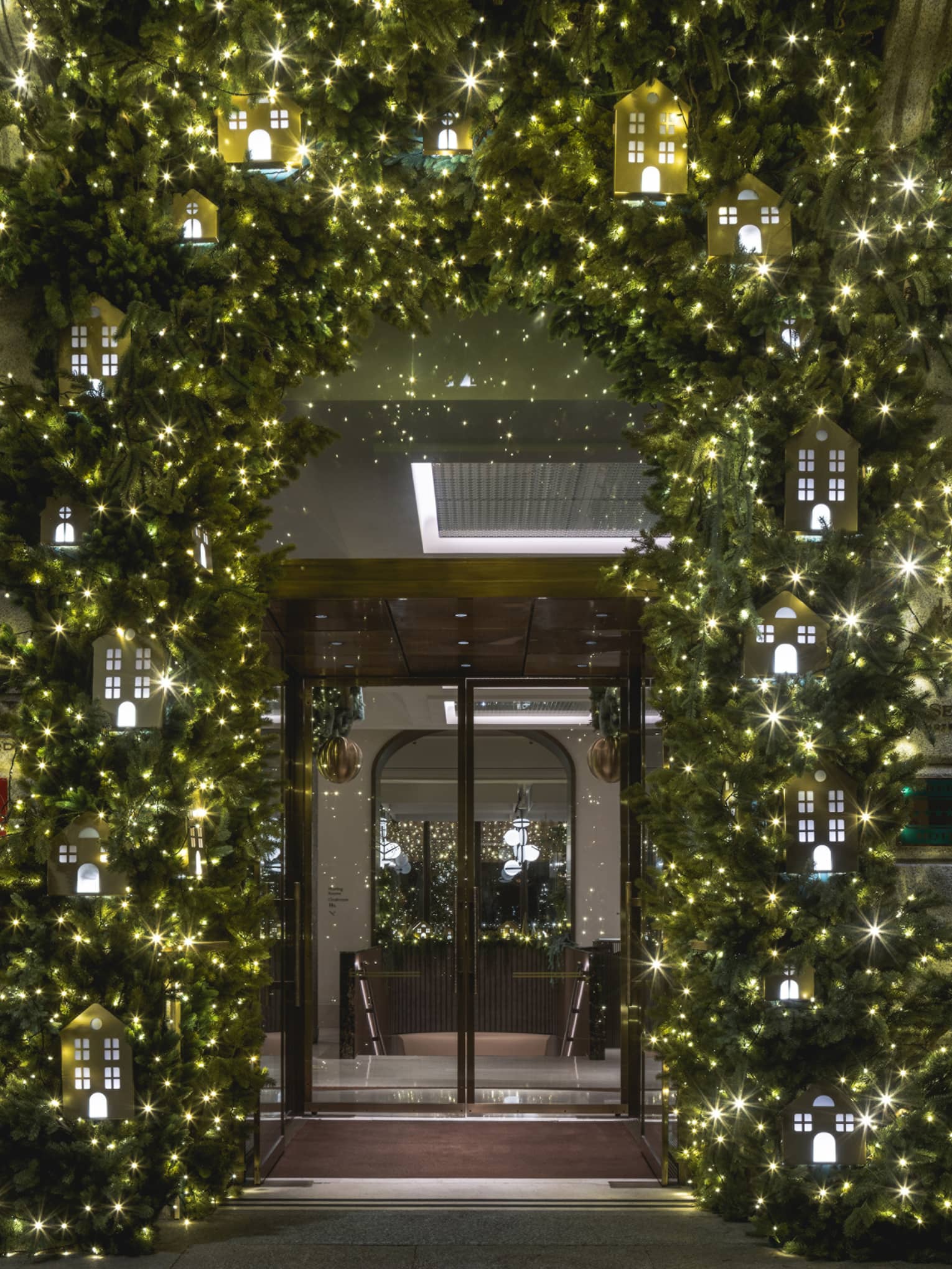 A door to a building, framed by festive greenery and holiday lights