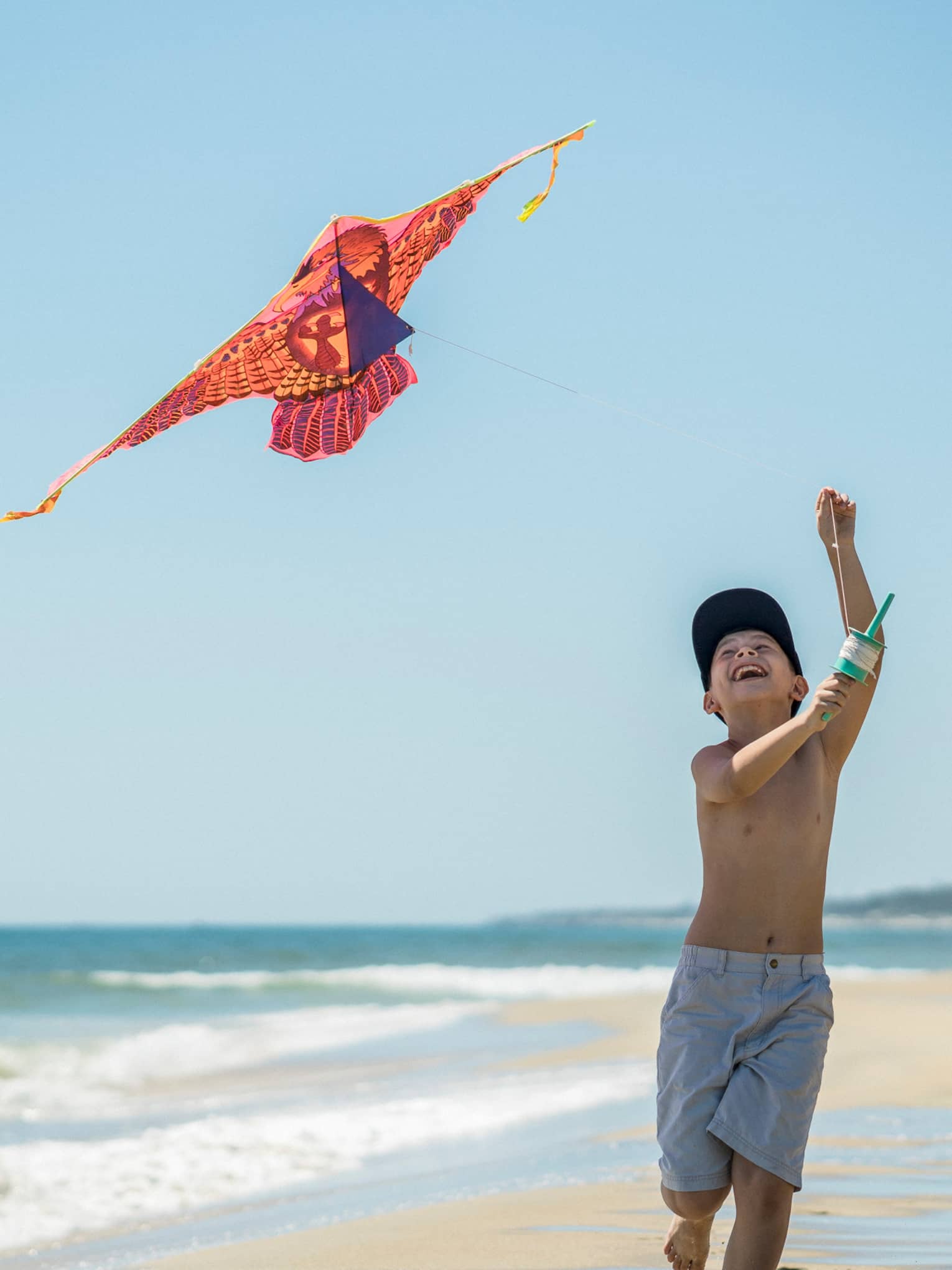 Smiling young boy flies colourful kite on beach by ocean
