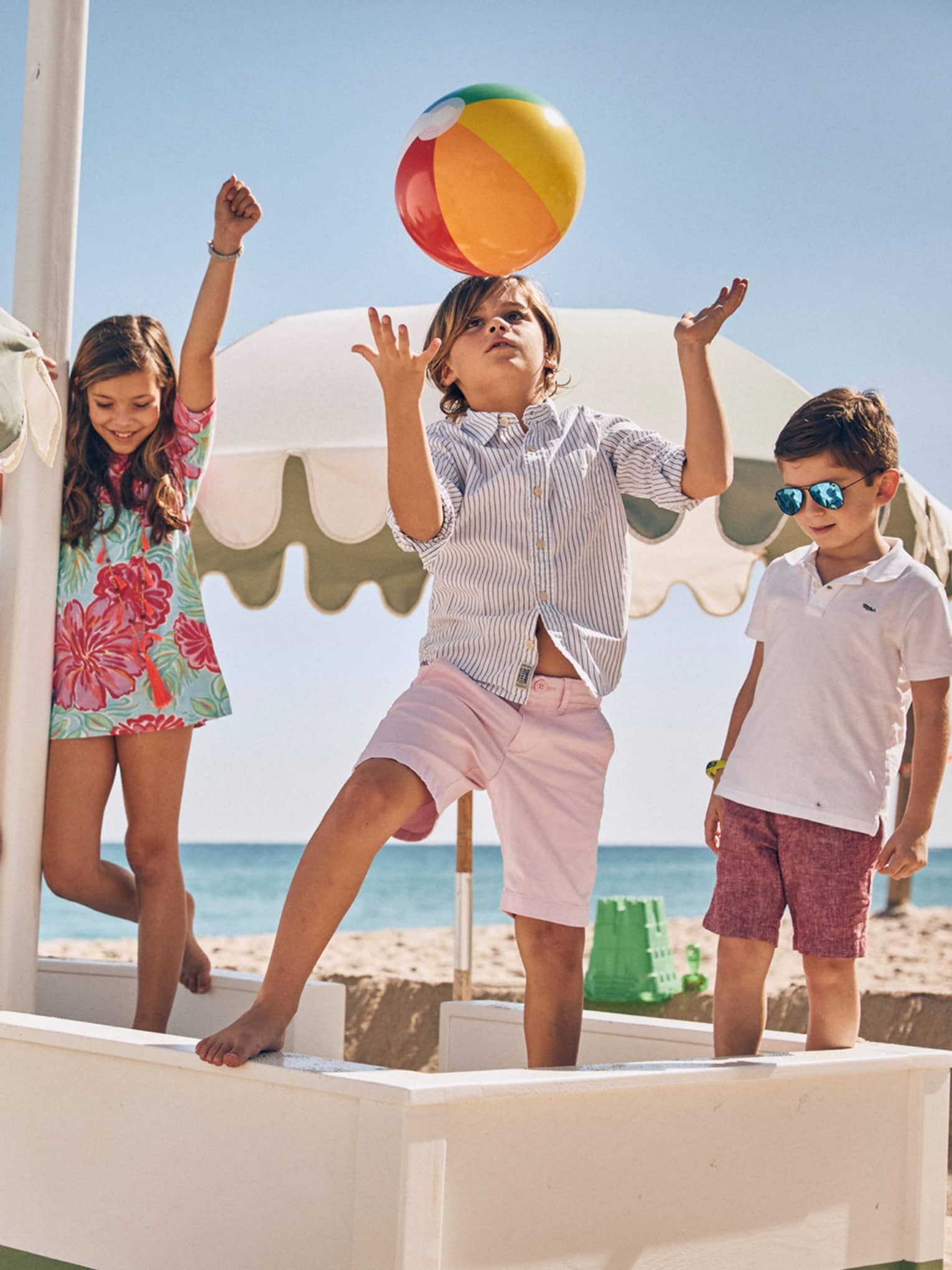 Four children playing on a sunny beach underneath white umbrellas