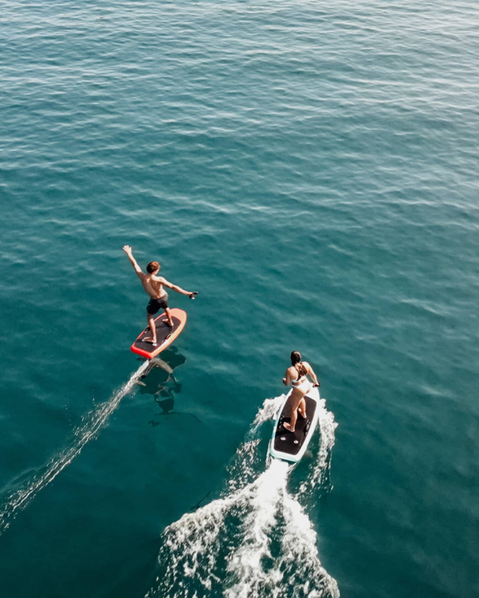 Aerial view of two people riding e0foil surfboards on blue-green water