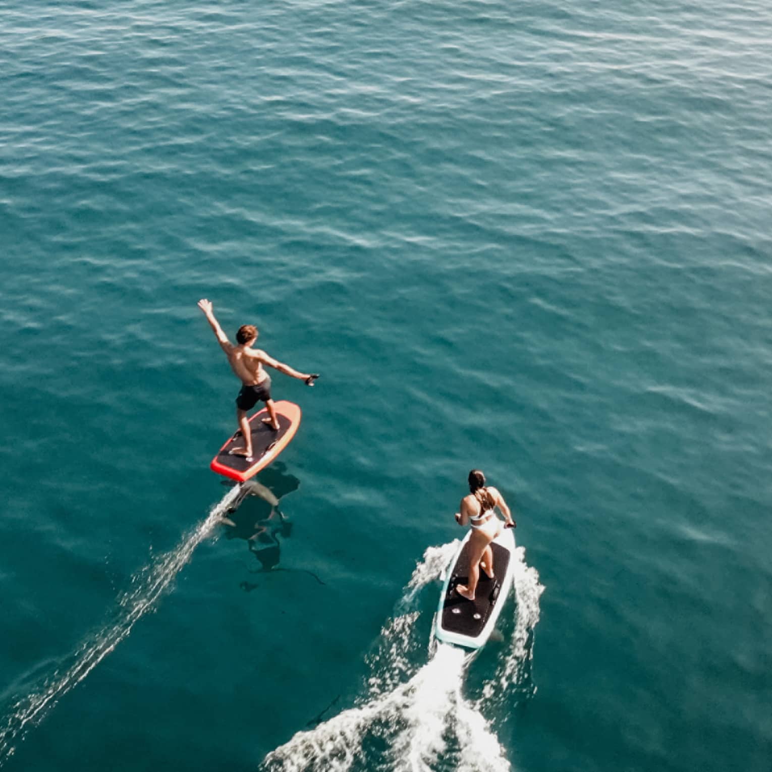 Aerial view of two people riding e0foil surfboards on blue-green water