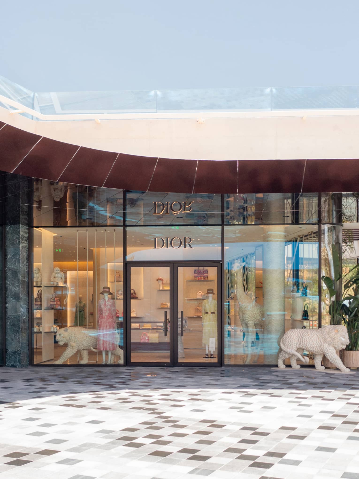Exterior of glass-walled DIOR boutique with front door flanked by white lion statues