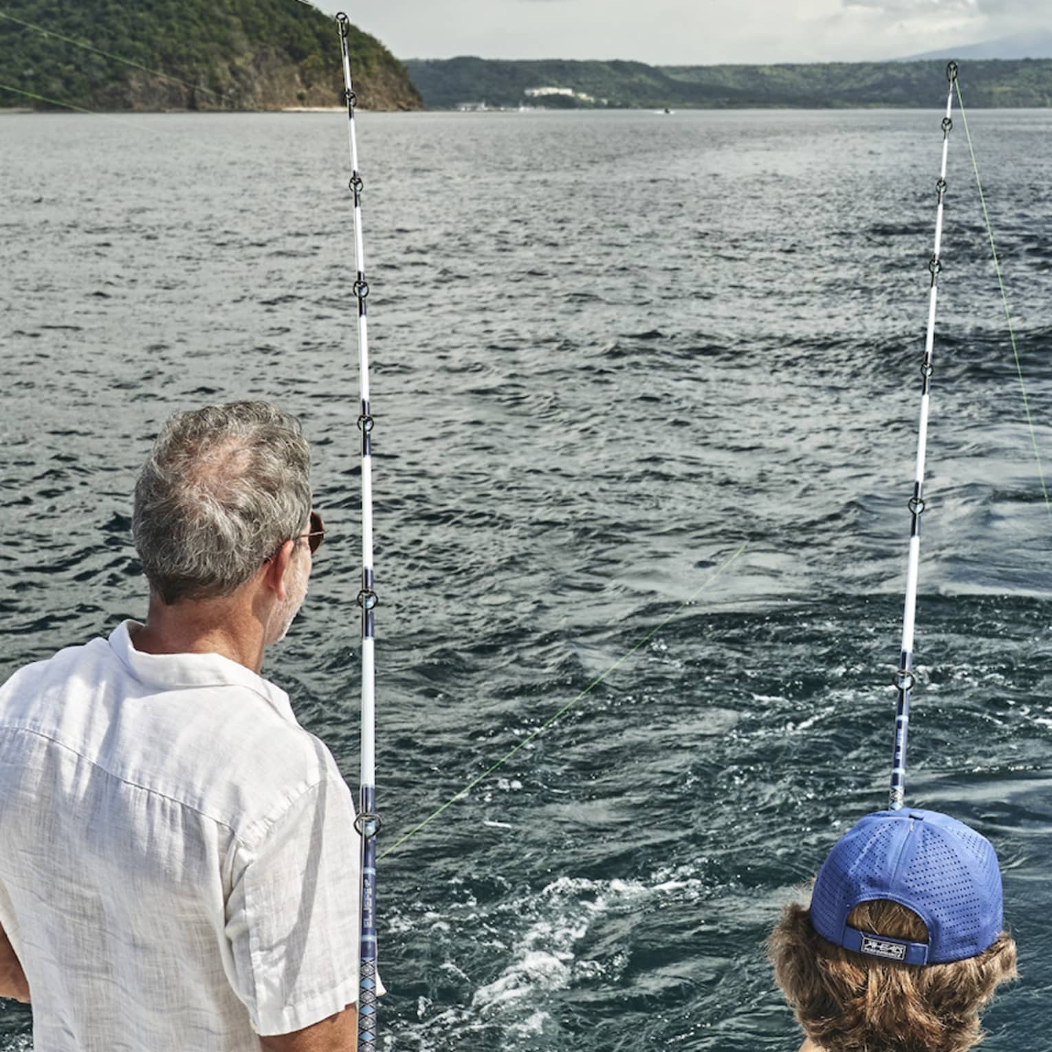 Three men of varying ages sit looking out at the water from the back of a boat outfitted with fishing rods