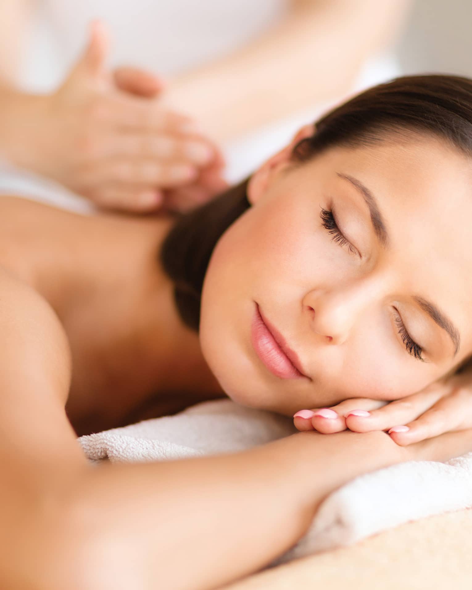 Woman lies on massage table, closes eyes. rests head on arms as spa staff massages back