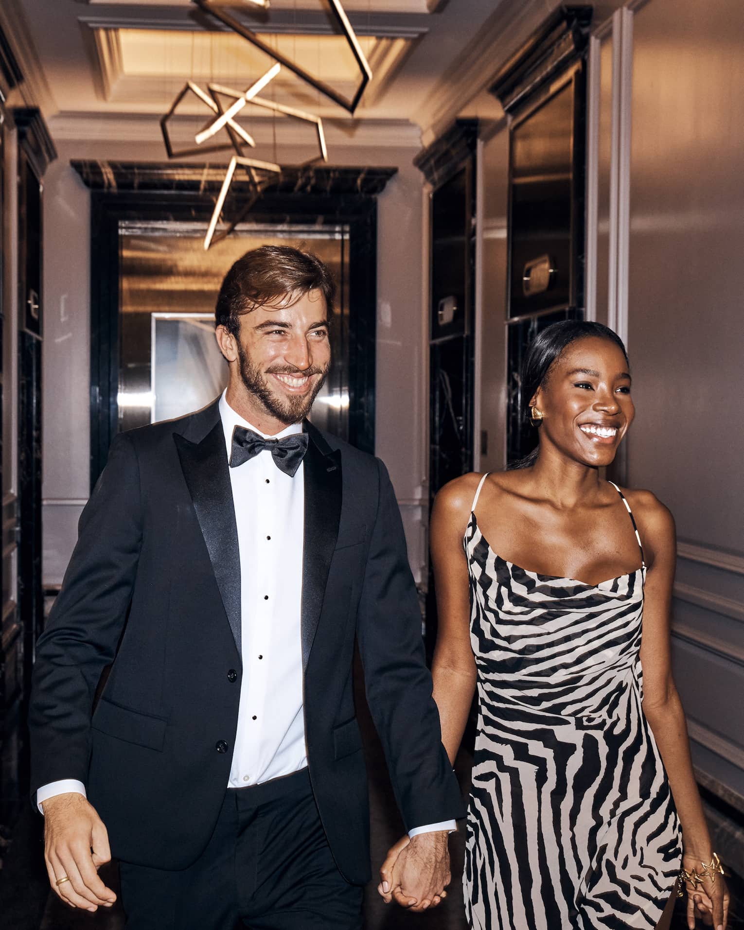 A man in woman in fine clothing walking down a hallway.