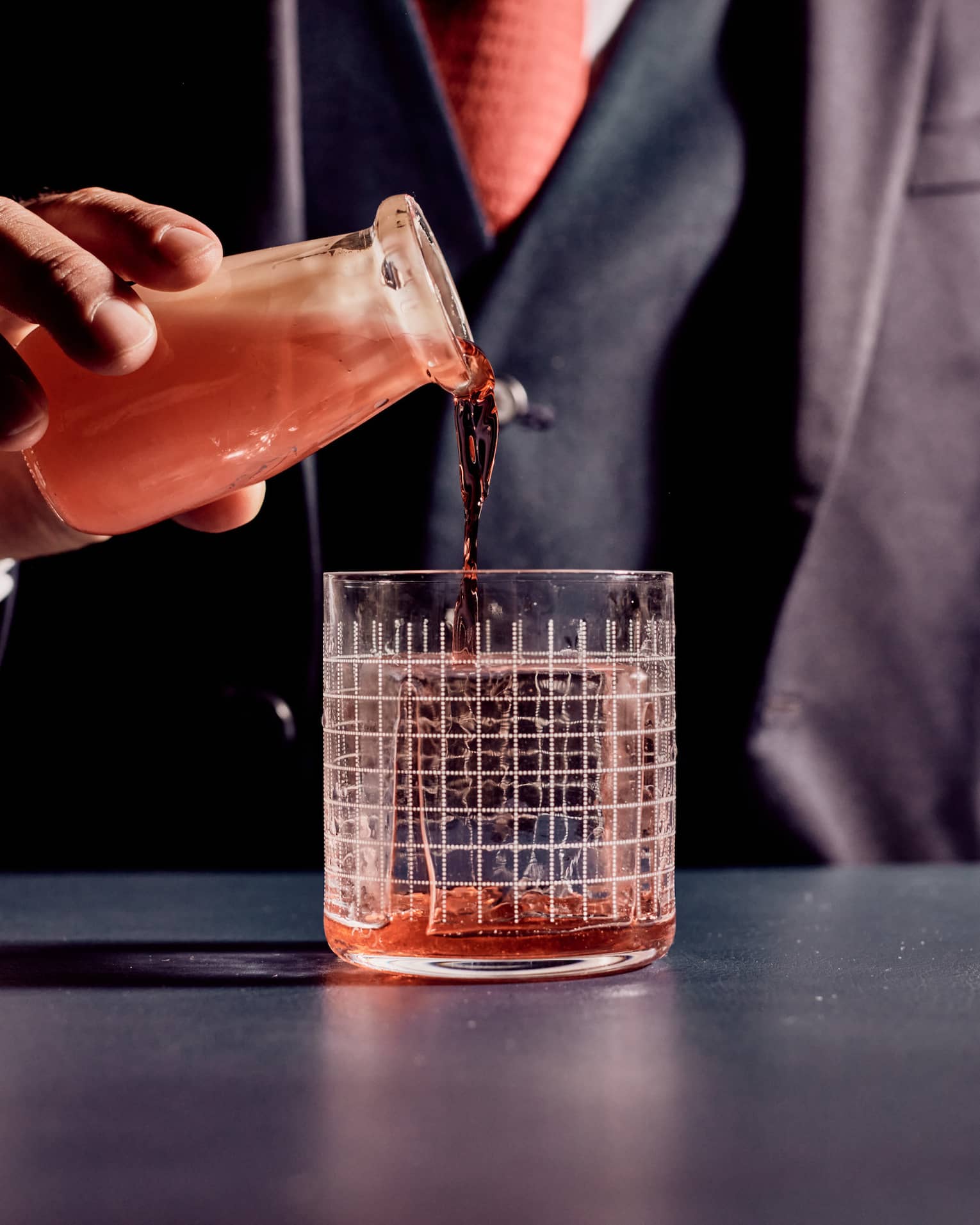 A bartender pouring a cocktail in a small glass.