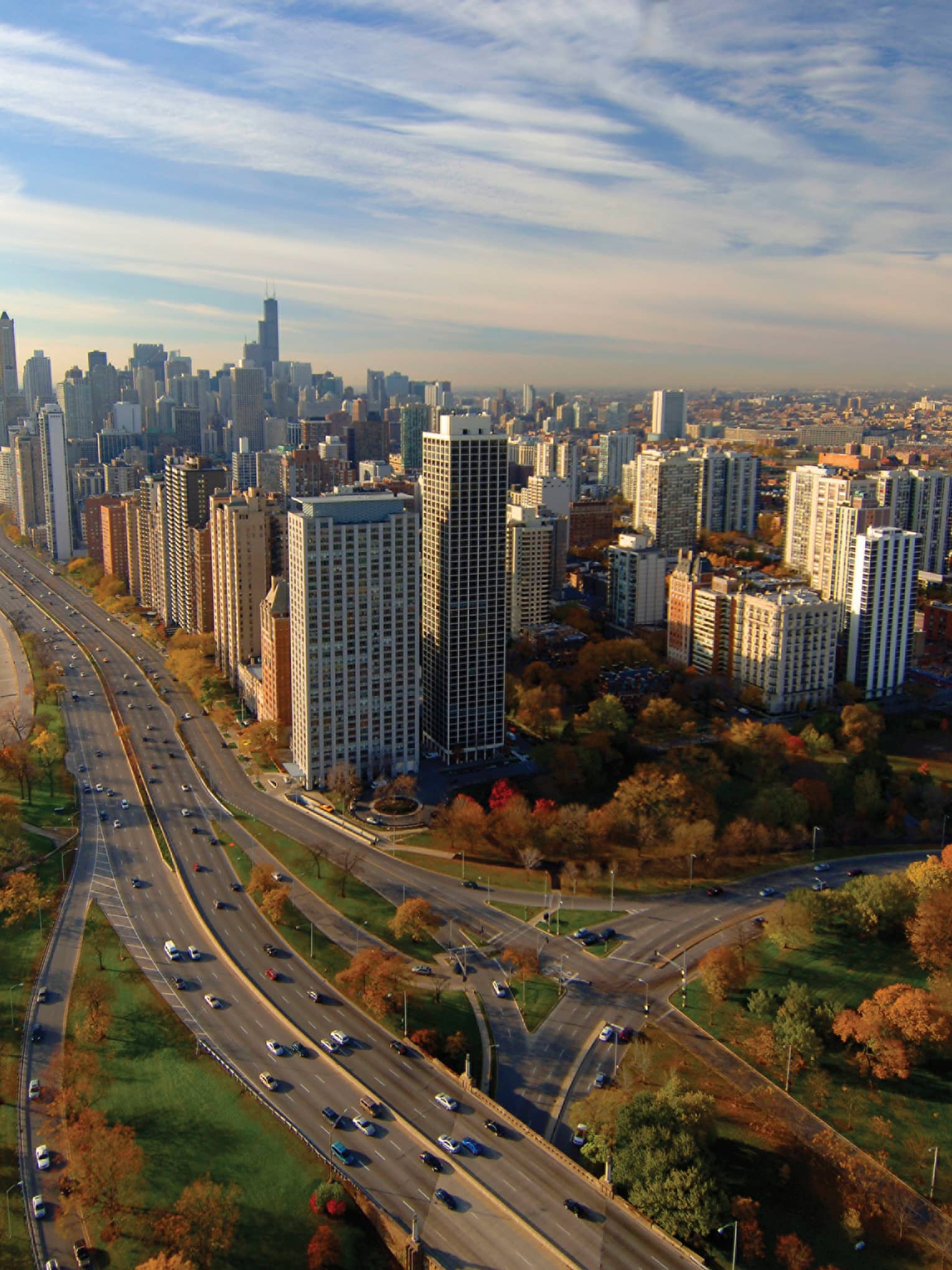 A road going through a city and trees with cars driving on it.