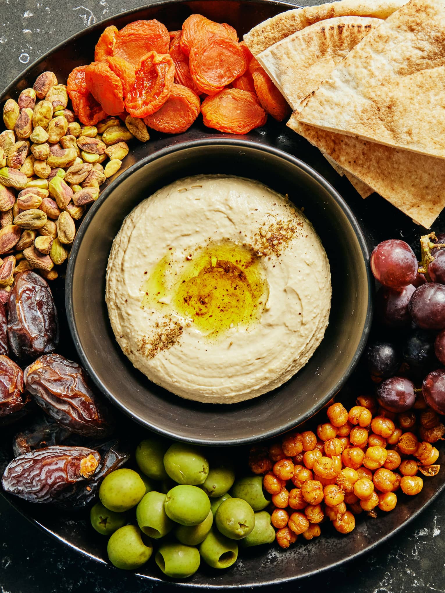 hummus, pita, fruit, nuts and olives on circular serving tray