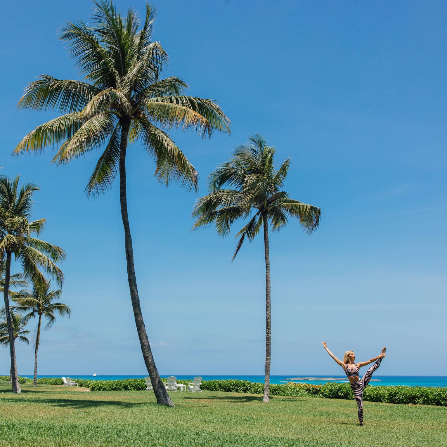A person doing a yoga pose outside near the ocean and palm trees