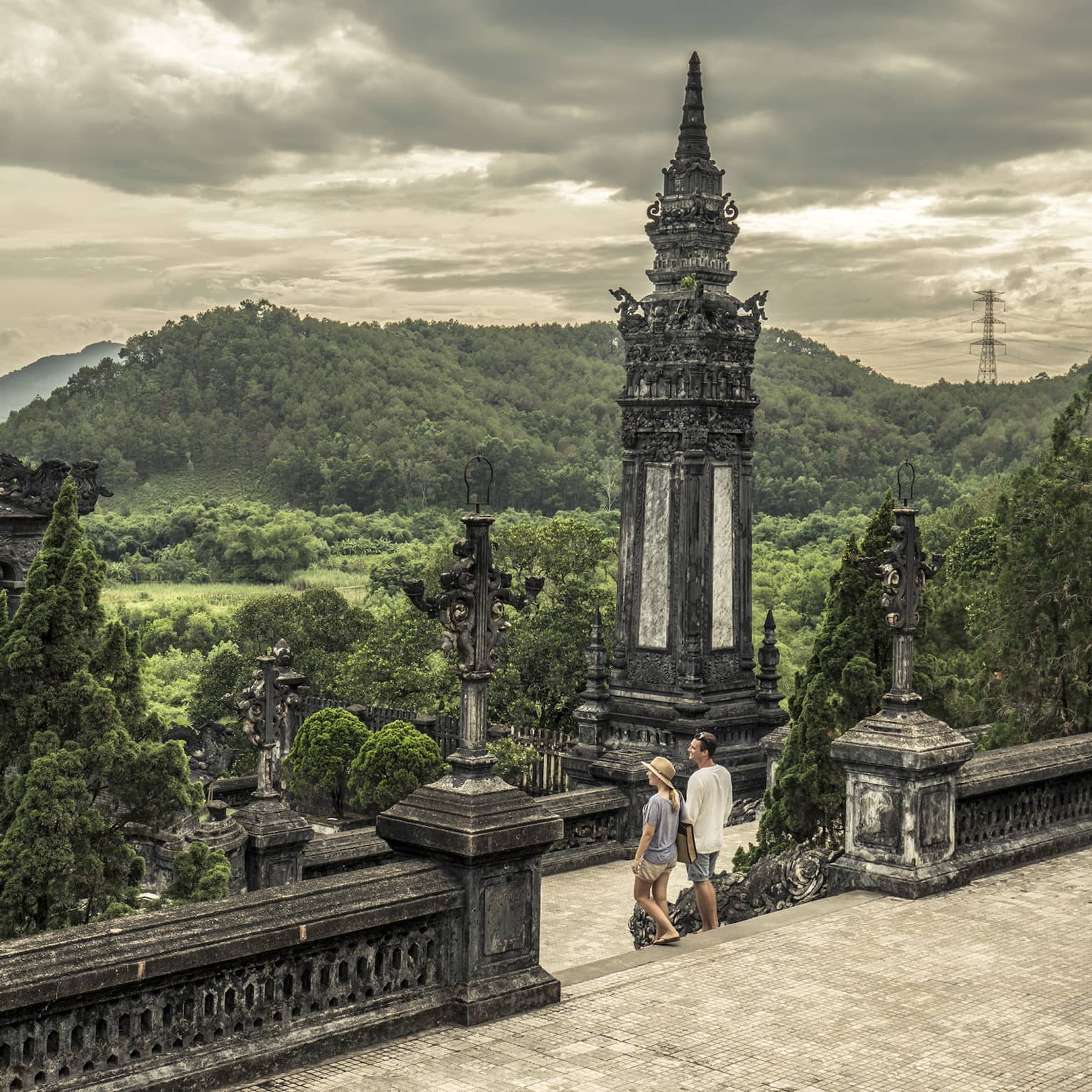 Man and woman walk down steps of historic Imperial City of Hue with stone towers, rolling hills