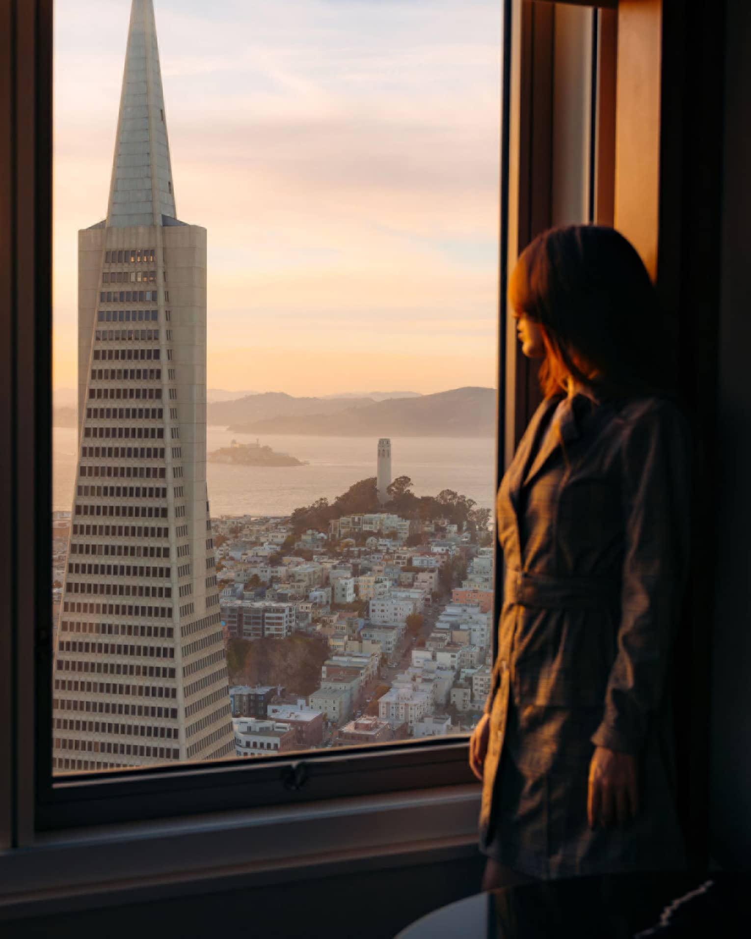 Woman gazes out hotel window to San Francisco cityscape