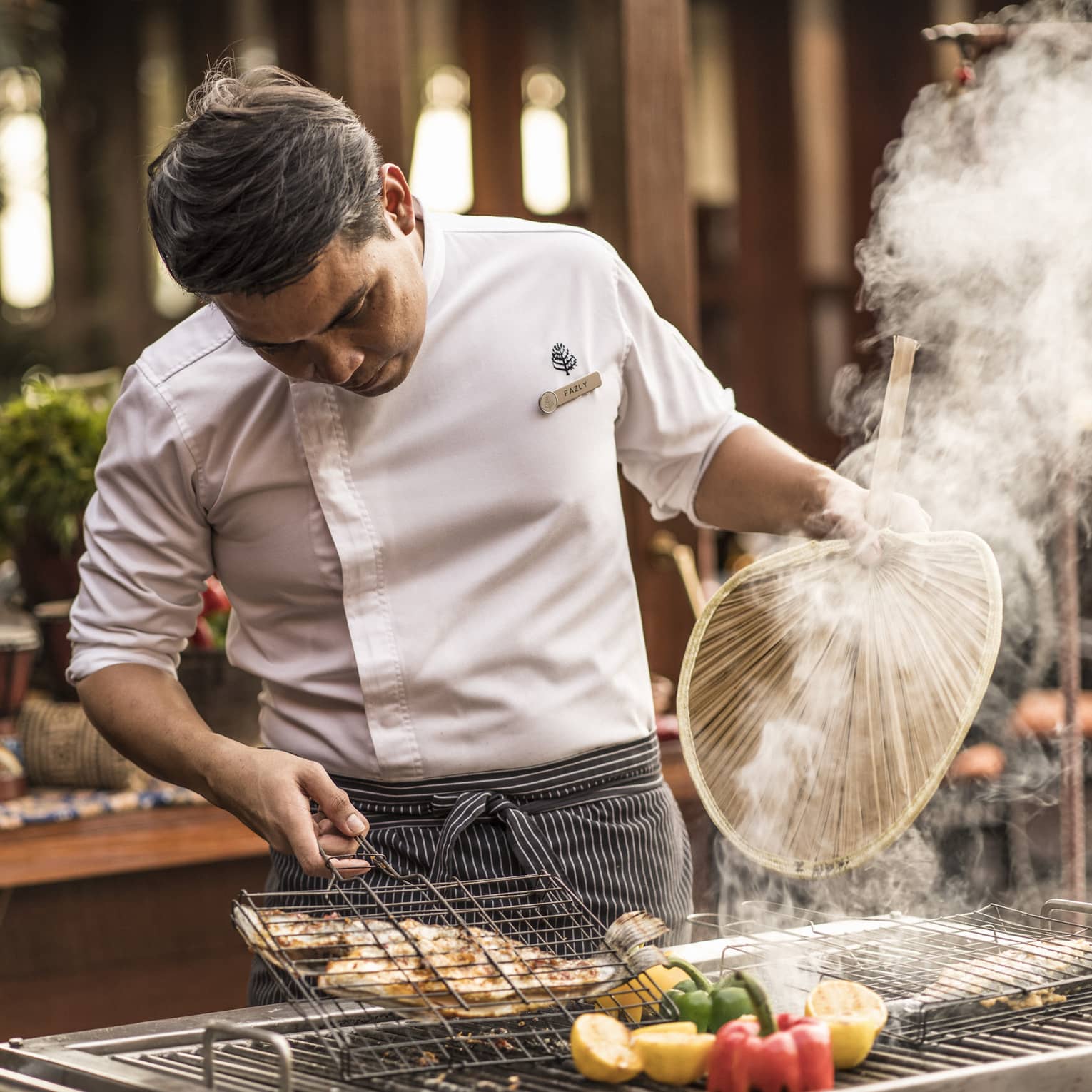 Ikan Ikan chef fans hot food over a grill with fresh peppers
