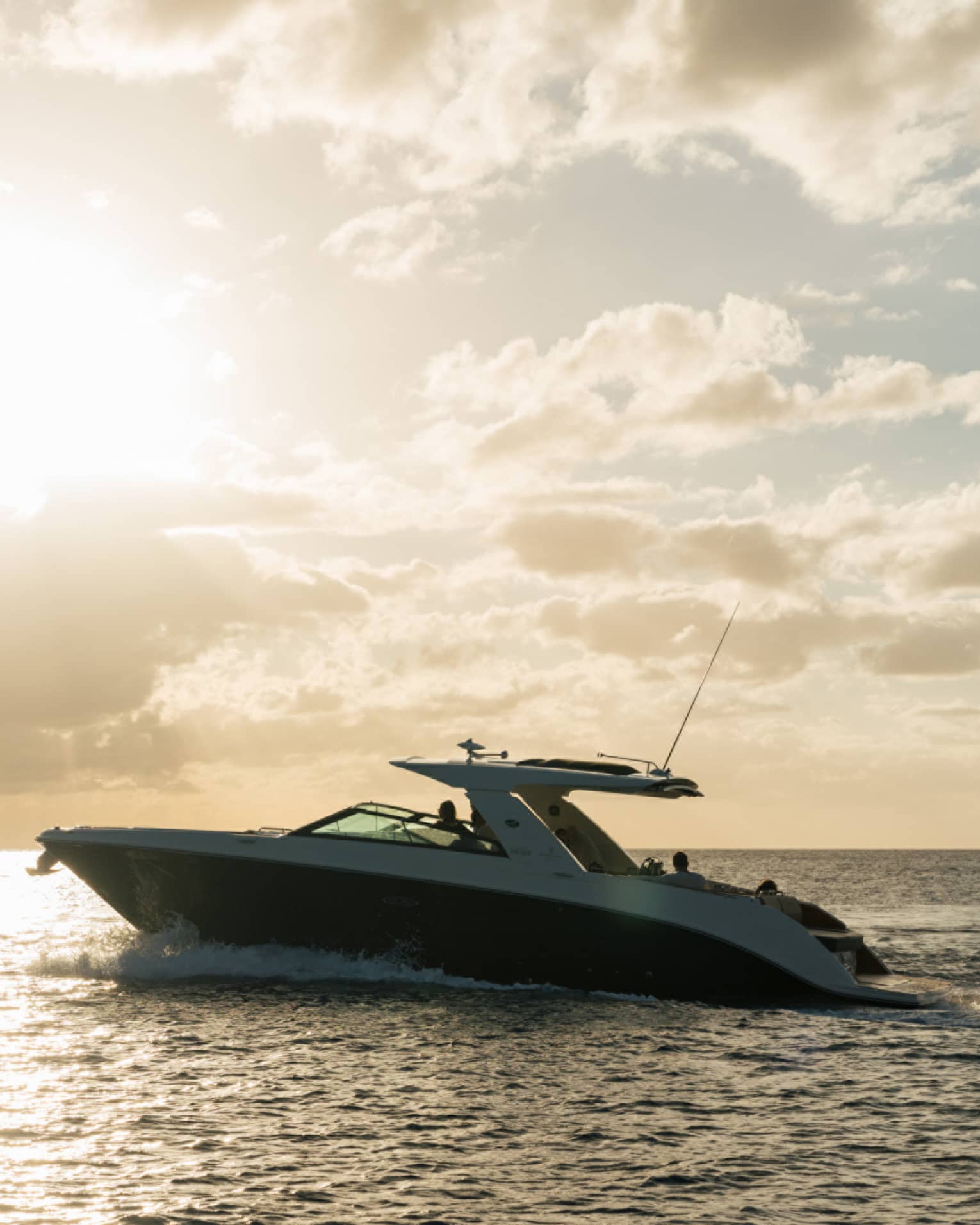 Luxury yacht in silhouette on open water under bright sunset bursting through clouds in an amber and blue skyscape.