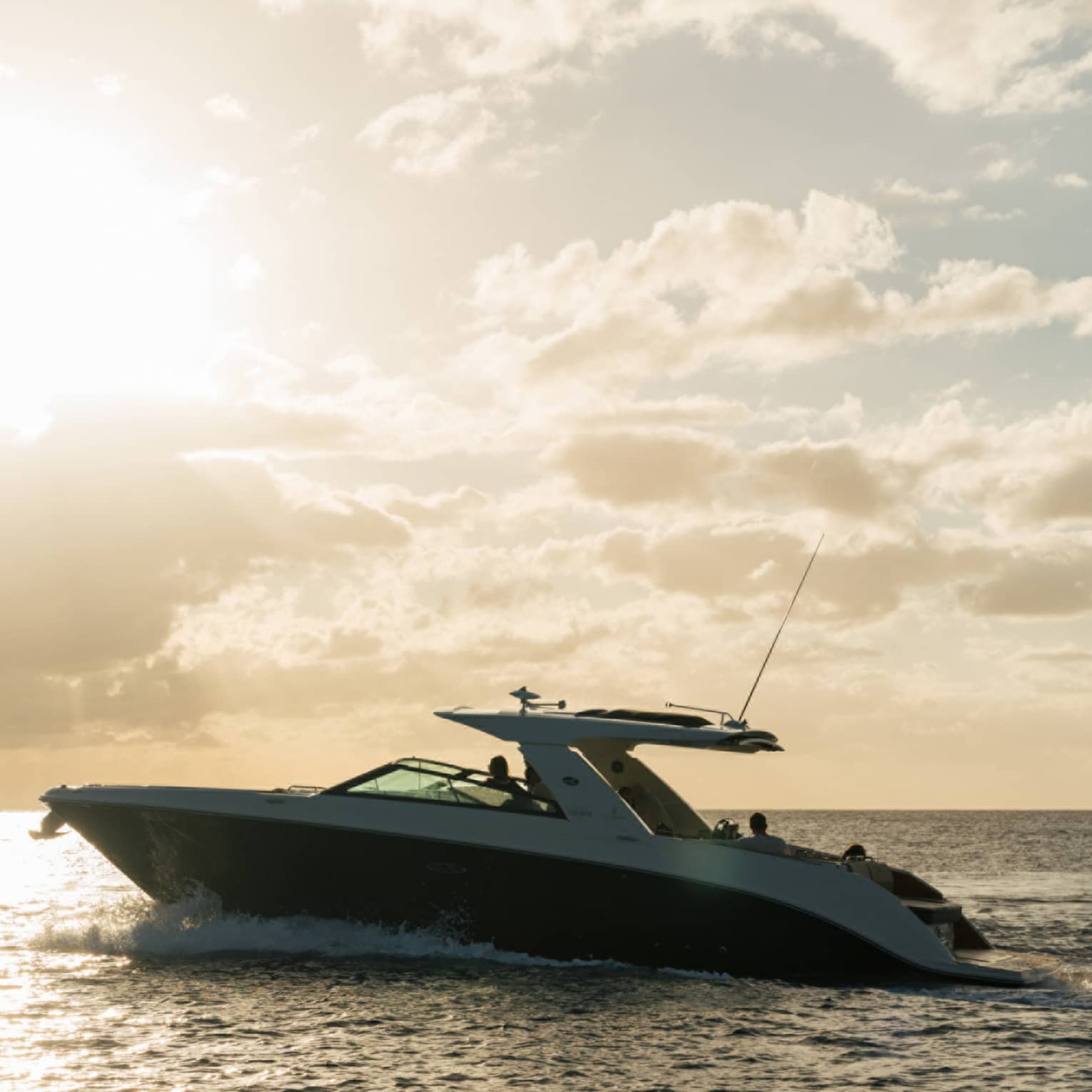 Luxury yacht in silhouette on open water under bright sunset bursting through clouds in an amber and blue skyscape.