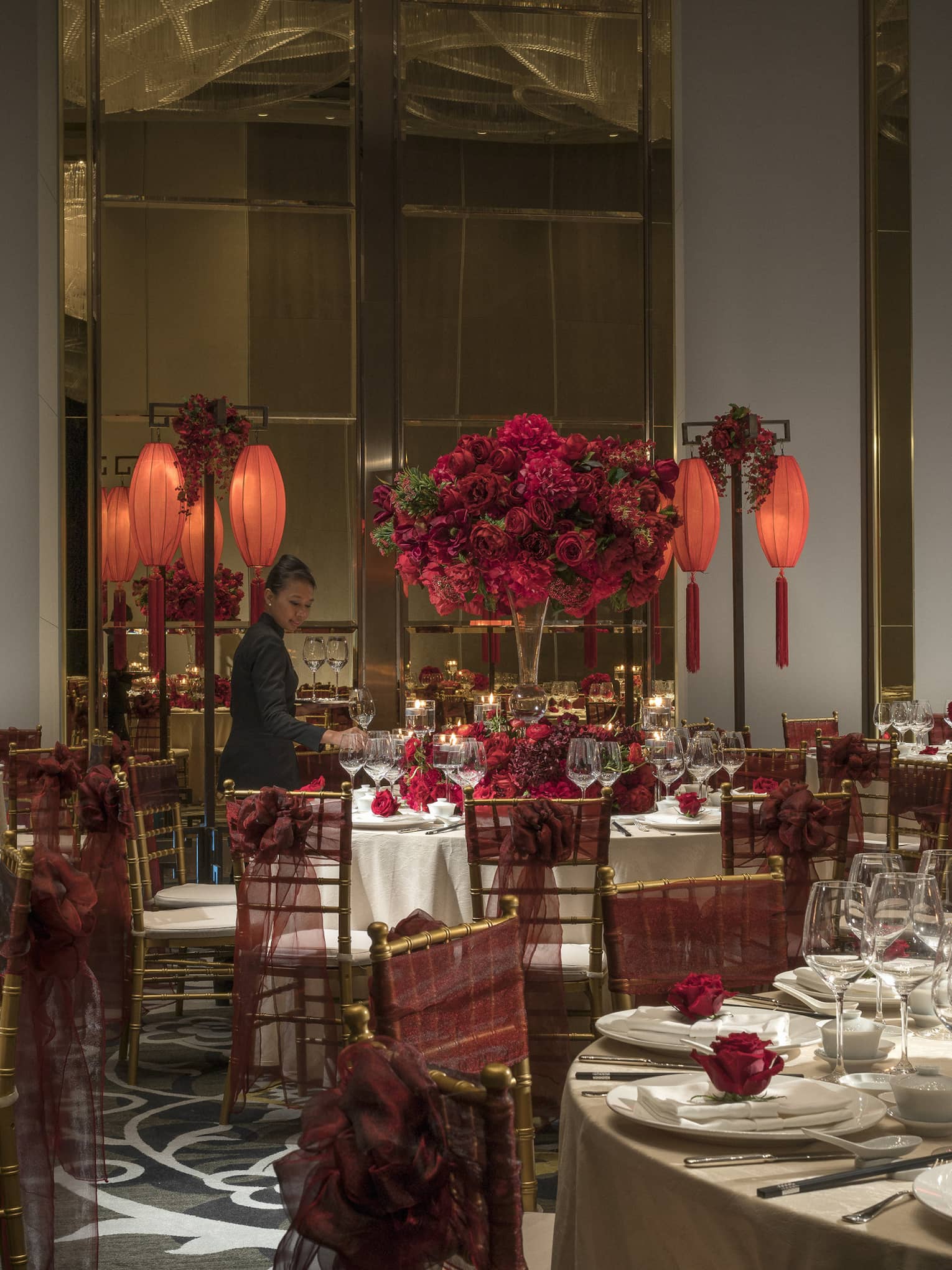 Hotel staff sets large round banquet tables with red flowers, lanterns for Chinese wedding