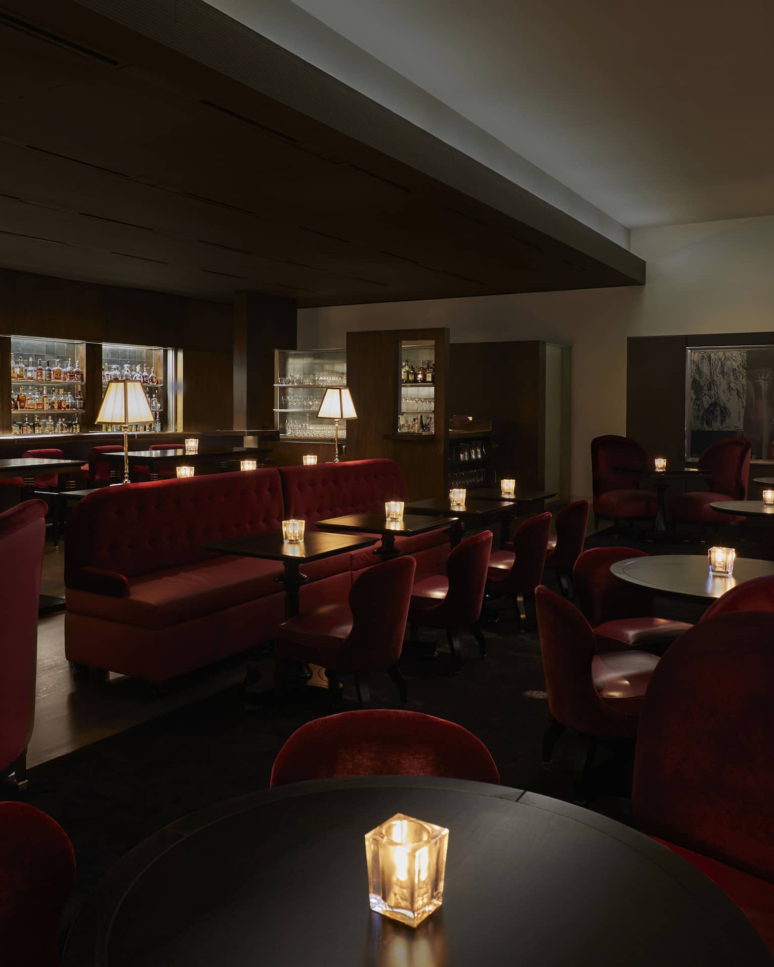 A dimly lit lounge with red chairs and a large selection of drinks behind a bar.