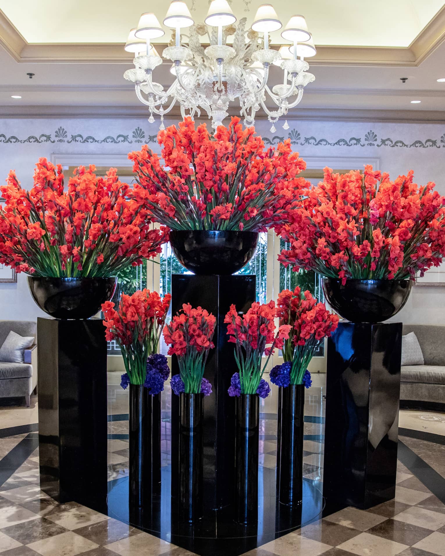 Hotel lobby, large red floral arrangements in black vases under crystal chandelier