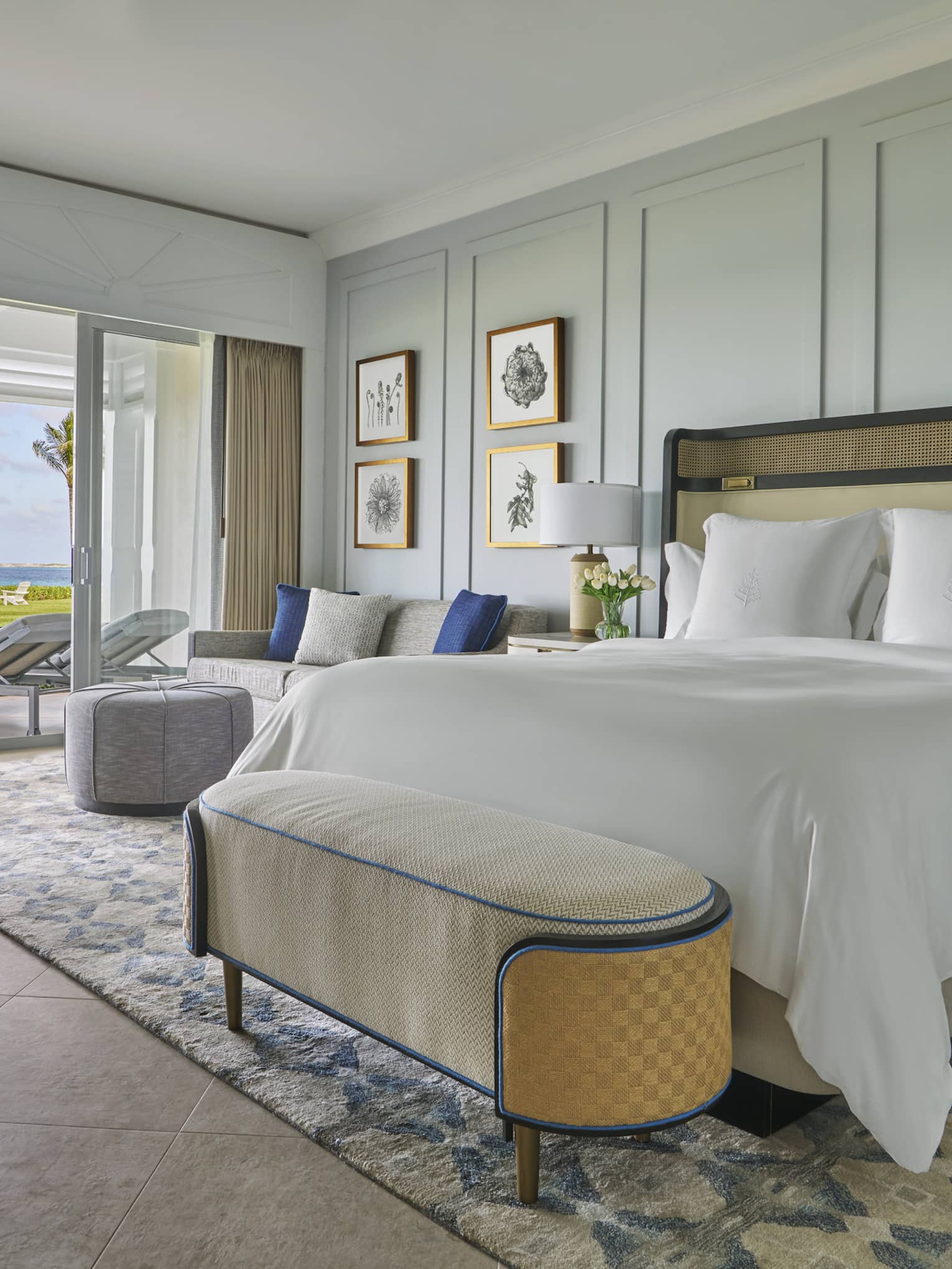Luxury oceanfront bedroom with a large bed, cozy seating and sliding glass doors opening to a private patio with lounge chairs 