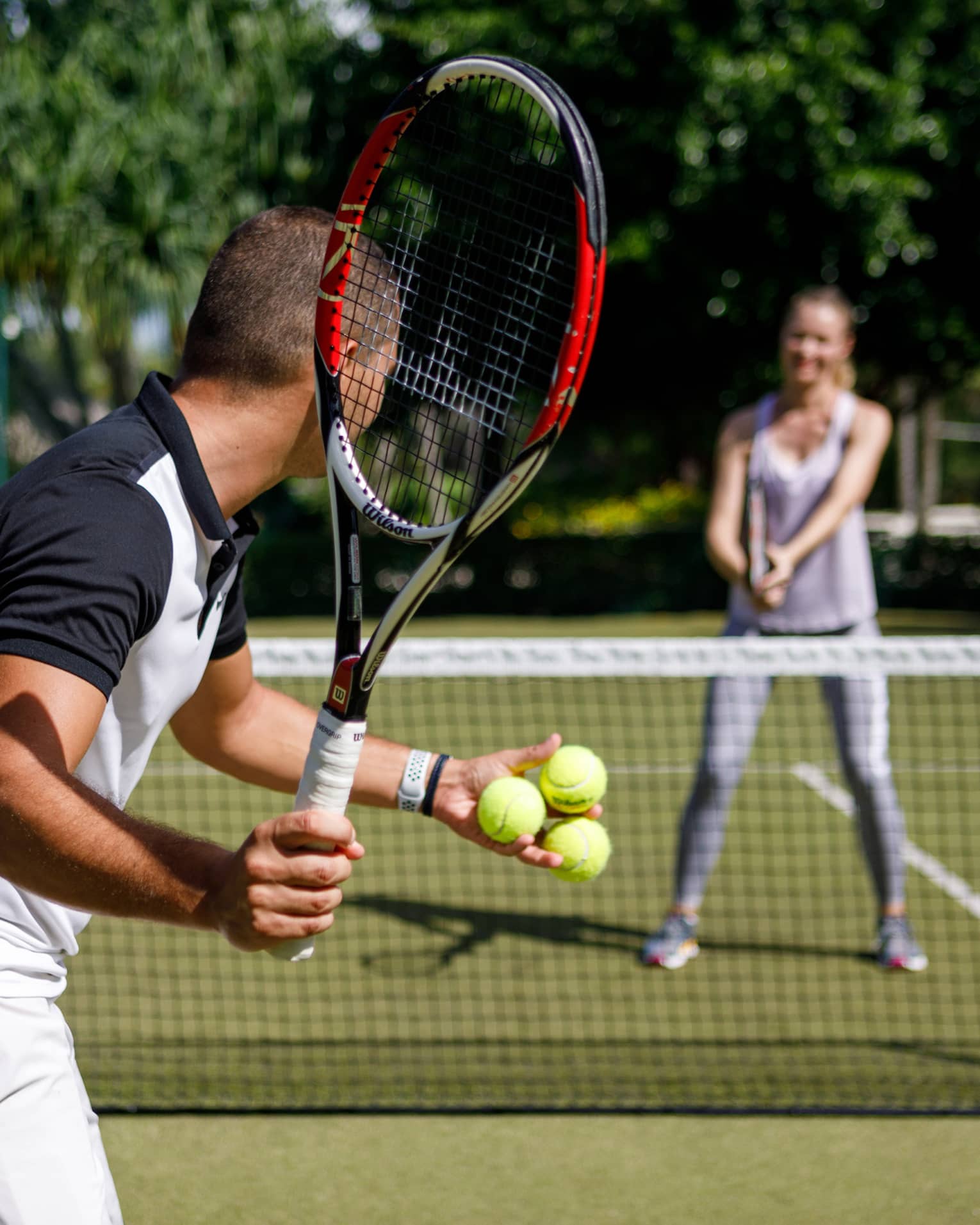 Couple playing tennis on court, man prepares to serve tennis balls to woman ready to swing