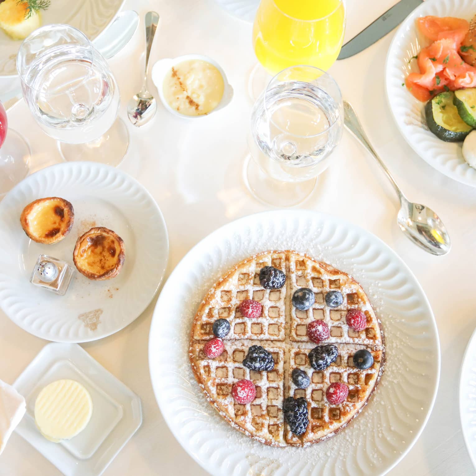 Aerial view of breakfast table with waffles, fresh fruit, pastries and juice in wine glasses