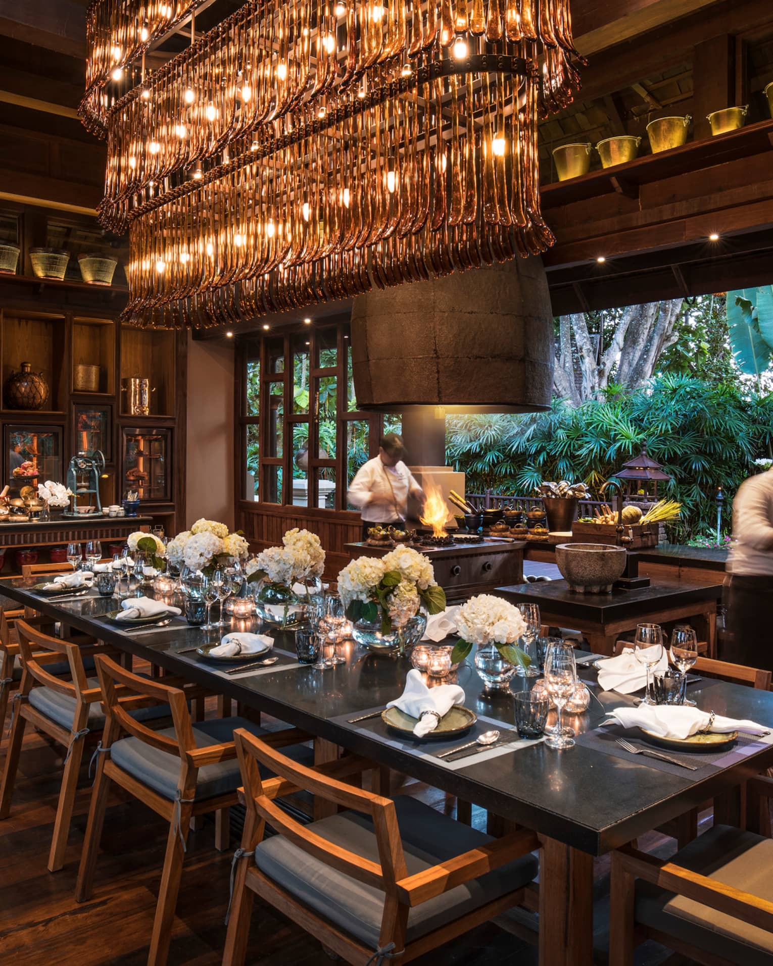 Large dining table under long rectangular crystal chandelier in Rim Tai restaurant, chefs in background