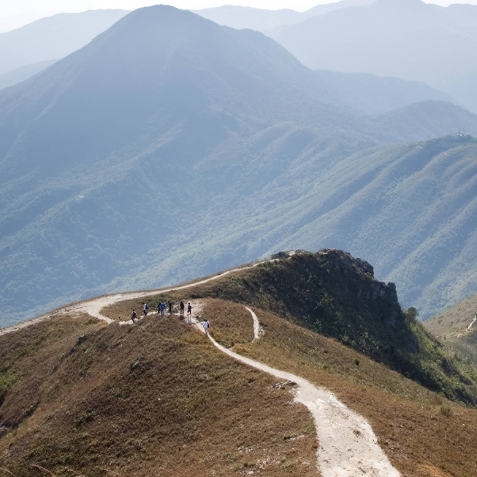 An aerial view of mountain ranges with a group of hikers walking on the path that runs along the ridge of the mountain tops.