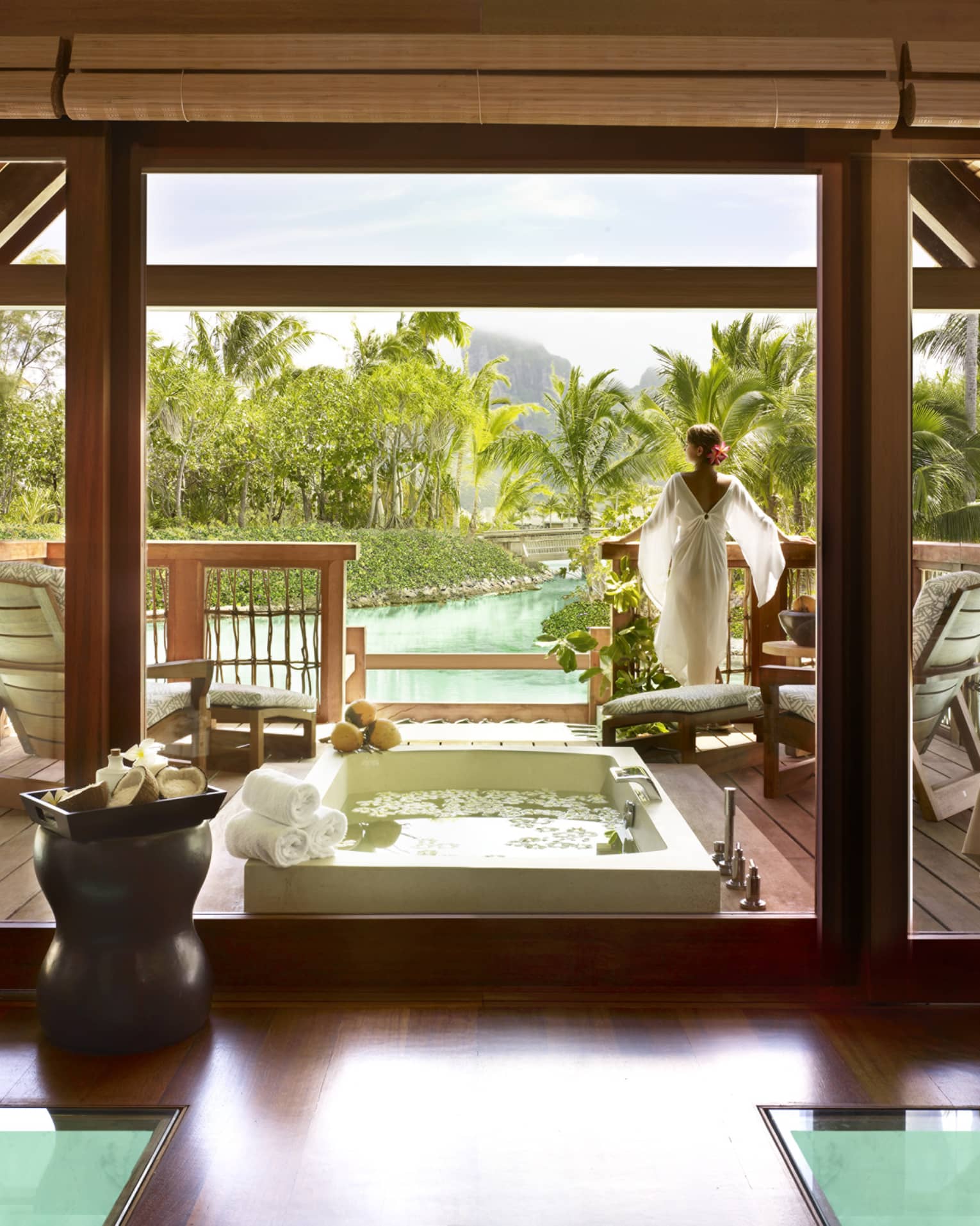 Woman wearing flowing white robe stands at edge of spa suite near plunge bath, couples massage beds