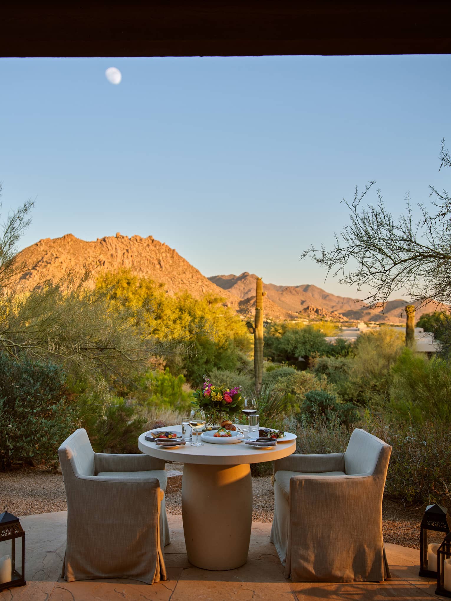 Two chairs and a table outside with lanterns and a view of the mountains.