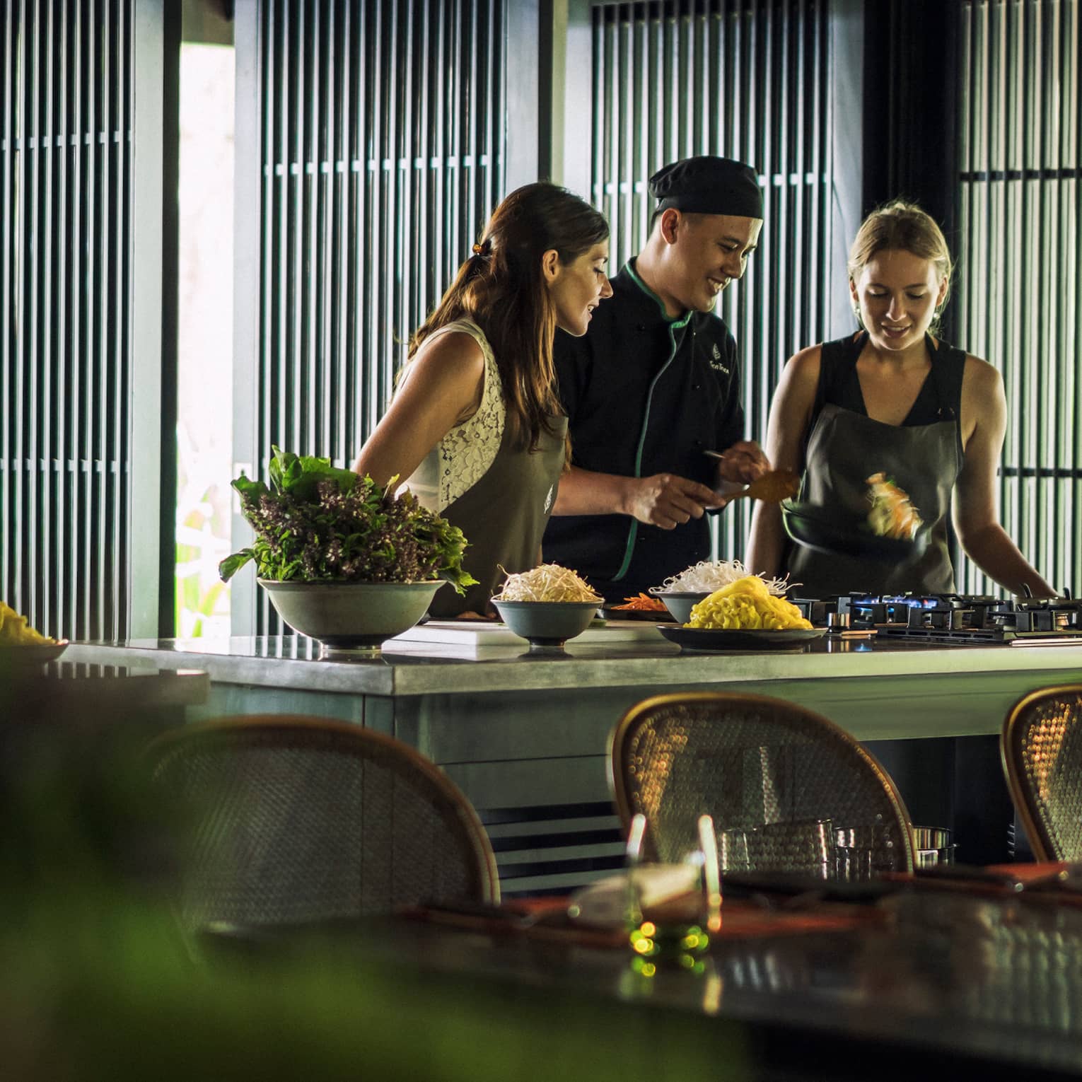 Chef, two women look at pan on kitchen range at Hoi An Cooking Academy 