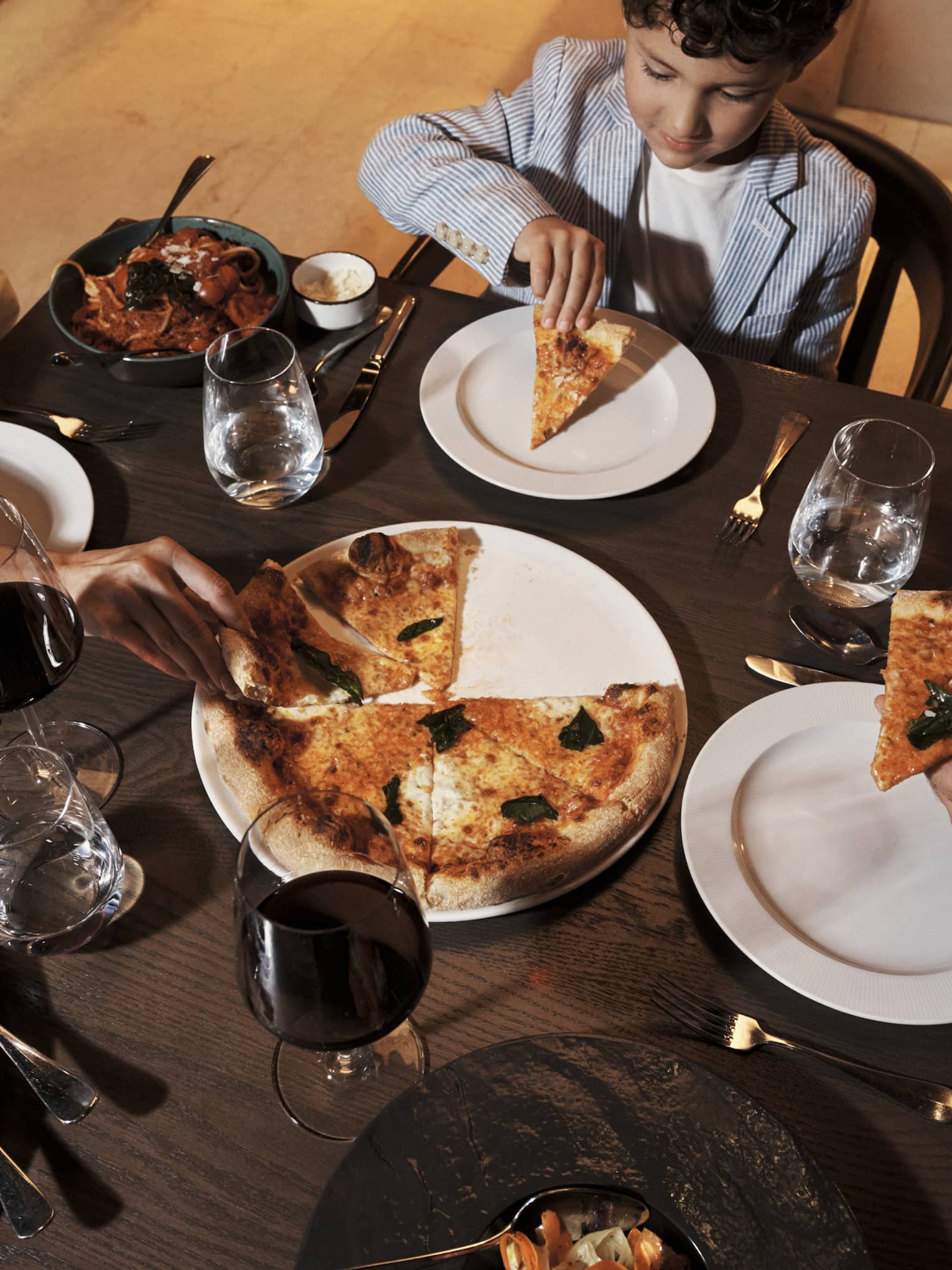 Guests sit at a small dining table set with dinner dishes, including pizza and fish.