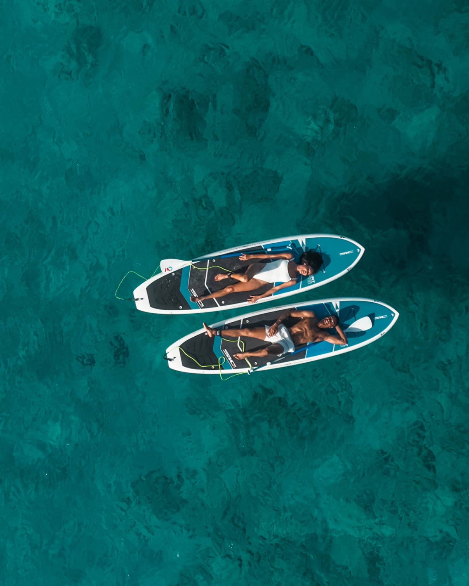 Two people lay on SUP paddleboards on the water